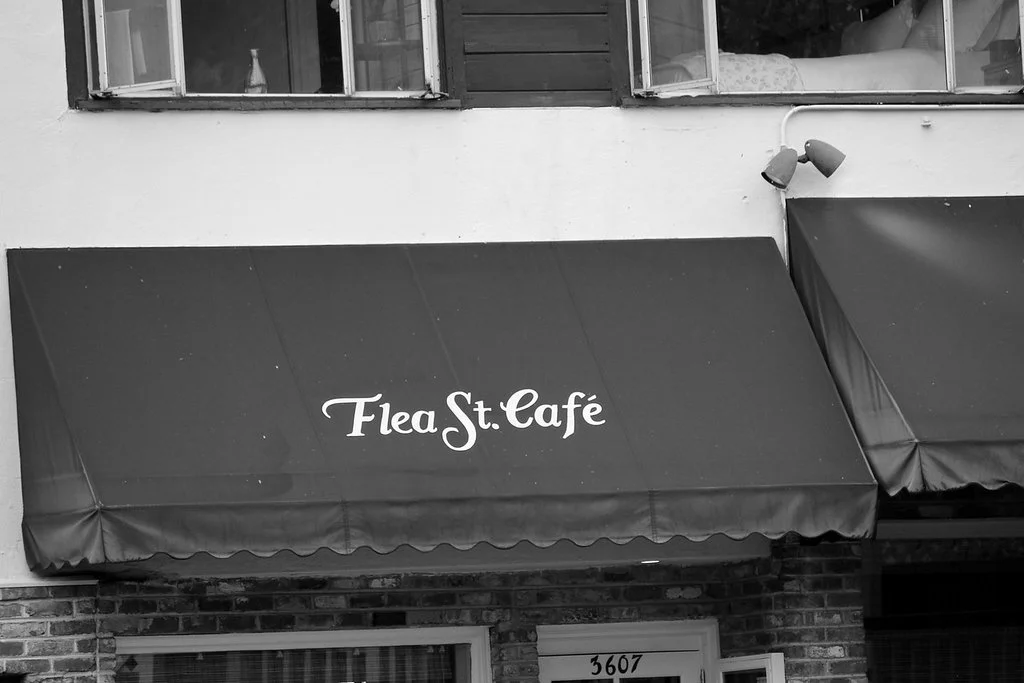 Black awning with white text that reads 'Flea St. Café' above a brick building entrance.