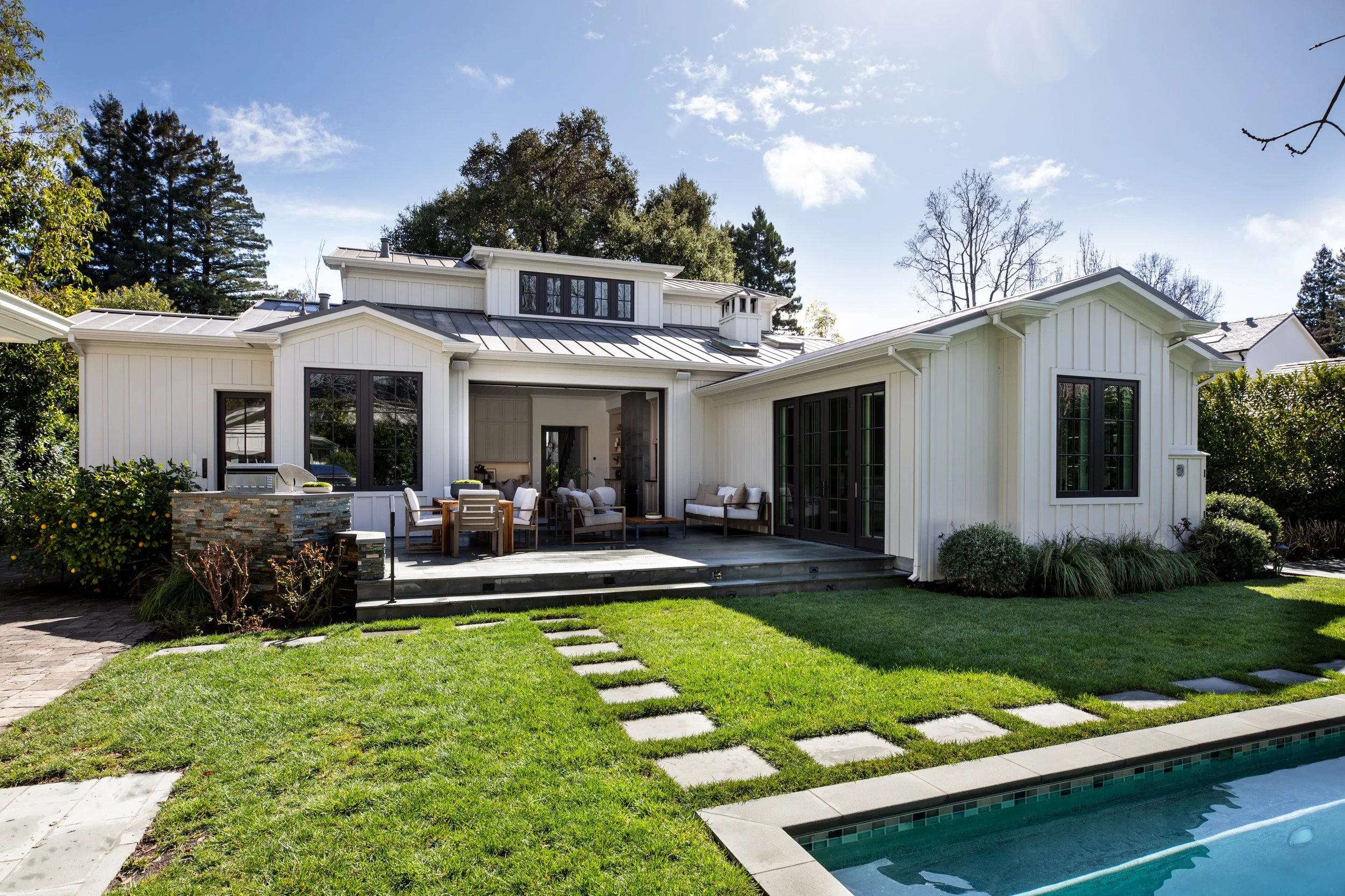 A modern white house with a backyard, outdoor seating area, and a swimming pool.
