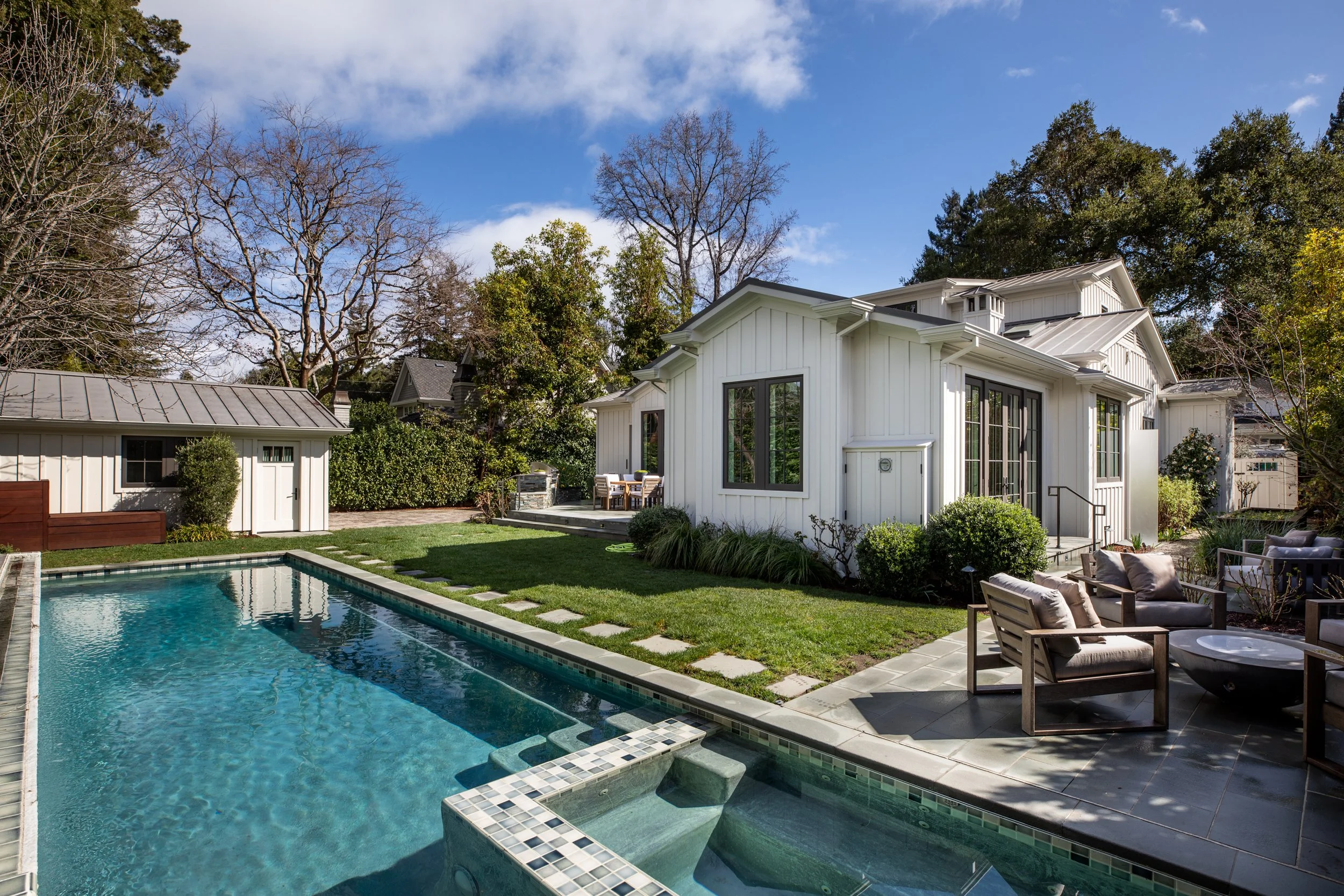 Backyard with a swimming pool, white house, outdoor seating, and trees.