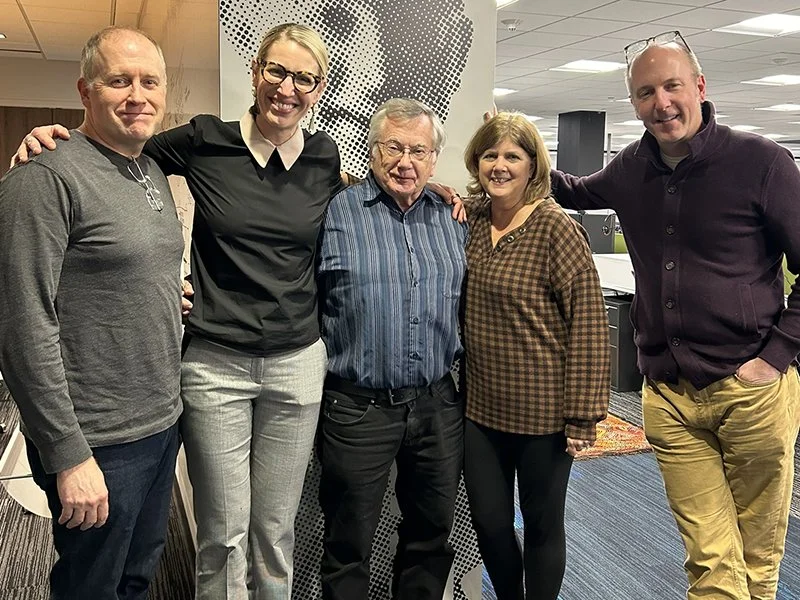 Five people standing together in an office, smiling and posing for the photo.