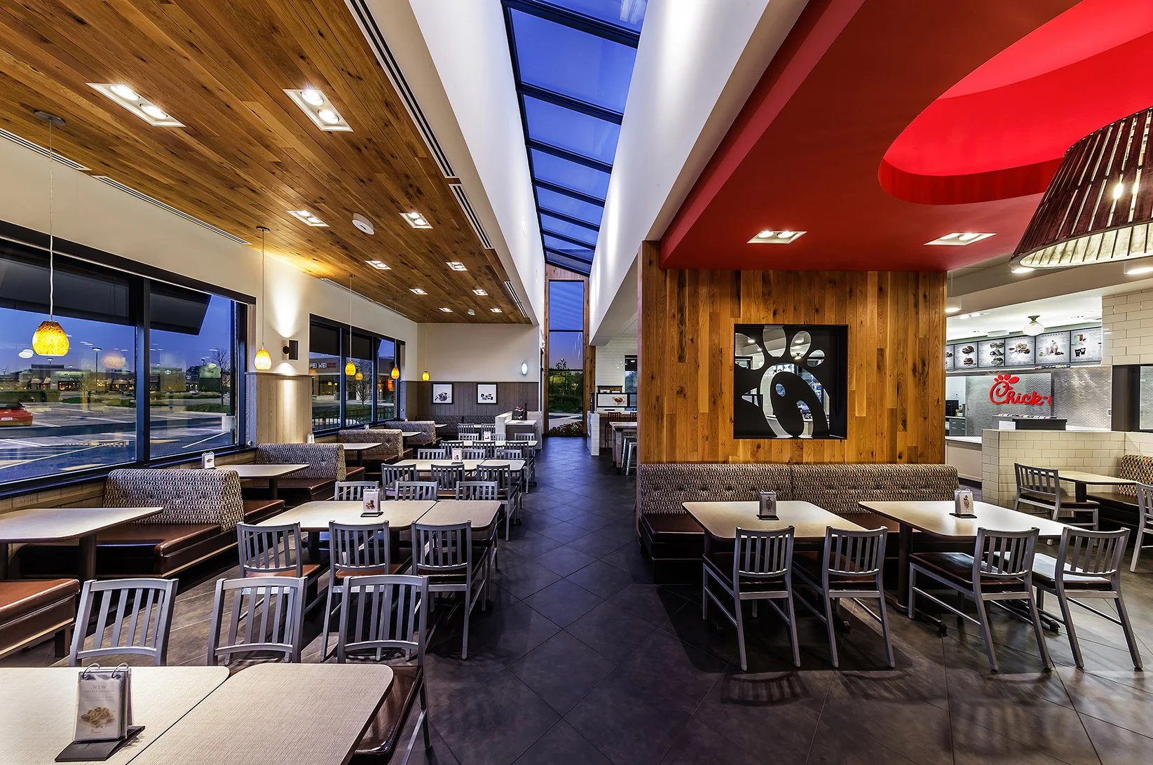 Interior of a modern fast-food restaurant with tables, chairs, and a counter. Large windows and skylights provide natural light.