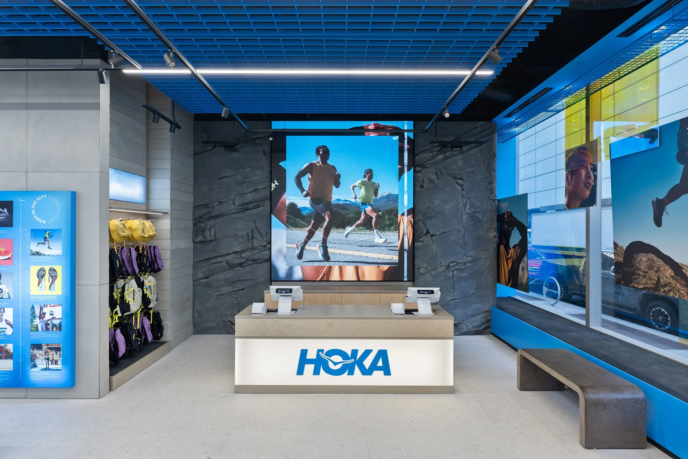 HOKA store interior with running gear, digital screens displaying runners, and branded display table.