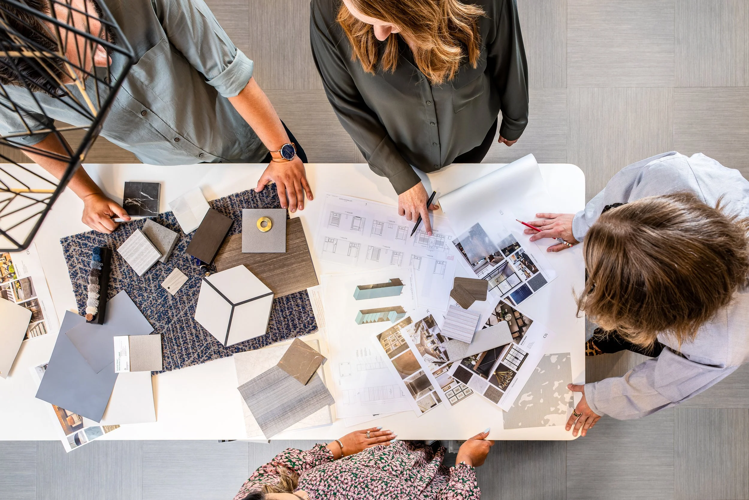 A group of people working on an interior design project at a table, reviewing color samples, decor swatches, sketches, and photographs.