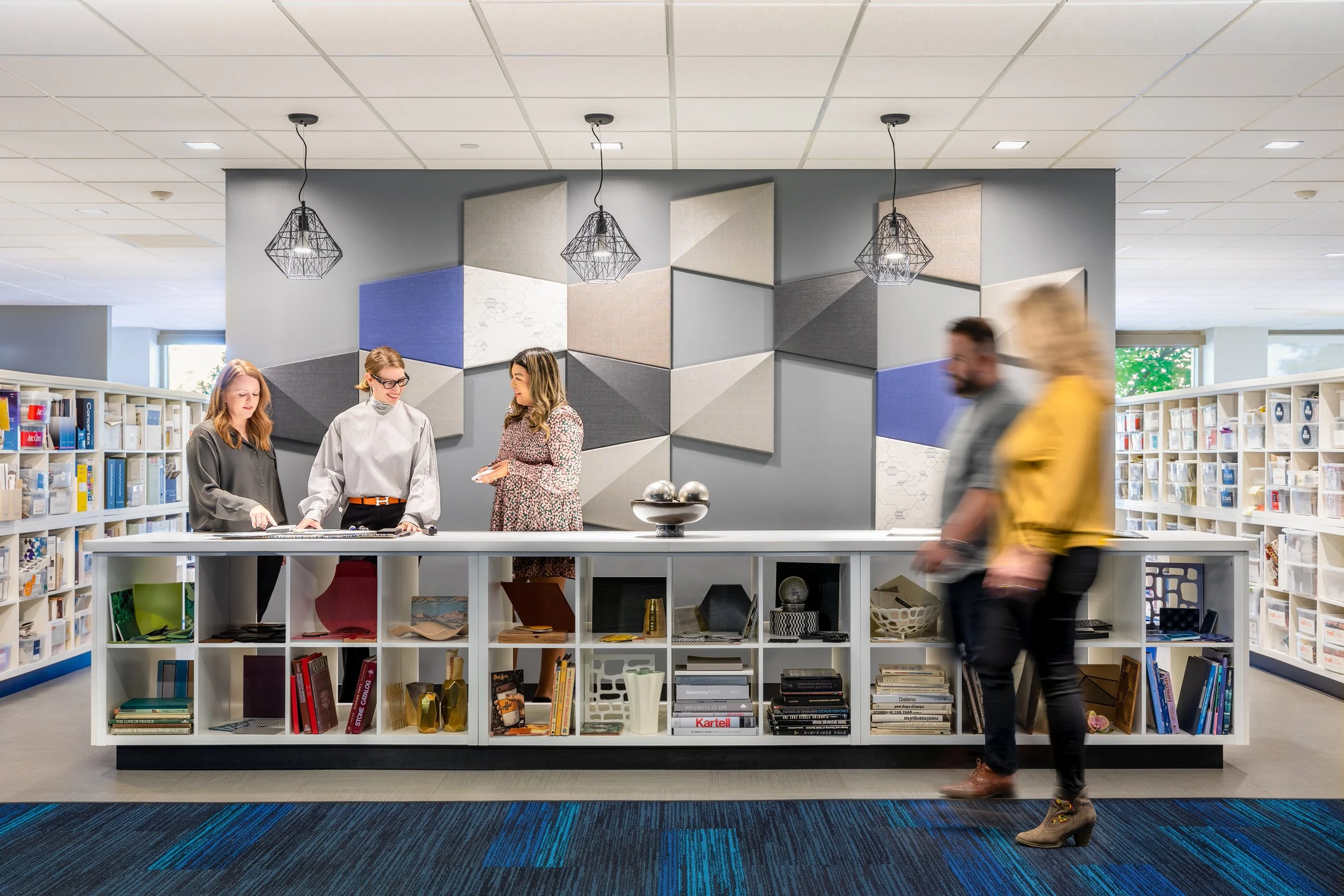 People browsing books and decorative items in a modern library or bookstore with a colorful geometric wall art installation and pendant lighting.