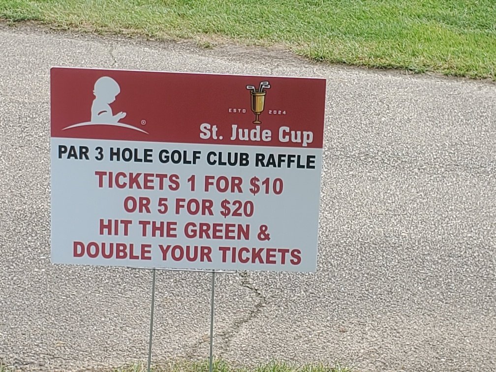 Sign advertising a par 3 hole golf club raffle called St. Jude Cup, with ticket prices of $10 for one or $20 for five, and a promotion to hit the green and double tickets.