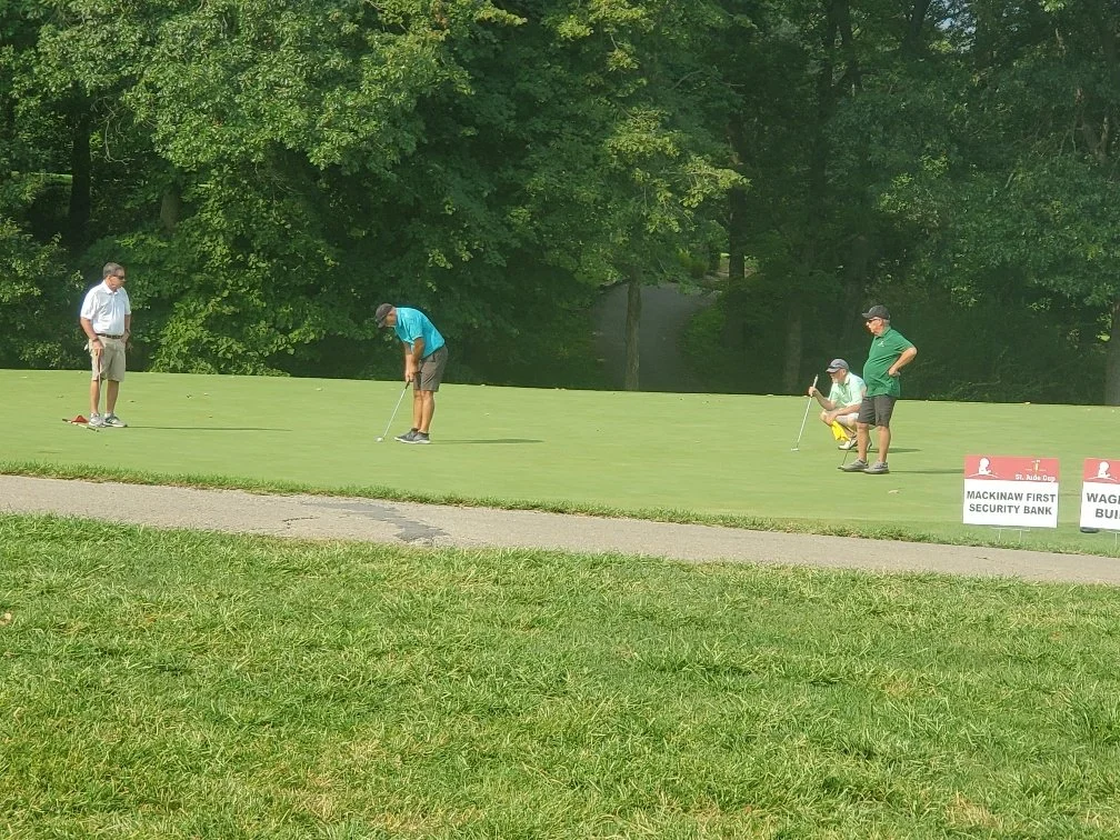 People playing mini golf on a putting green with signage in the background and trees surrounding the area.