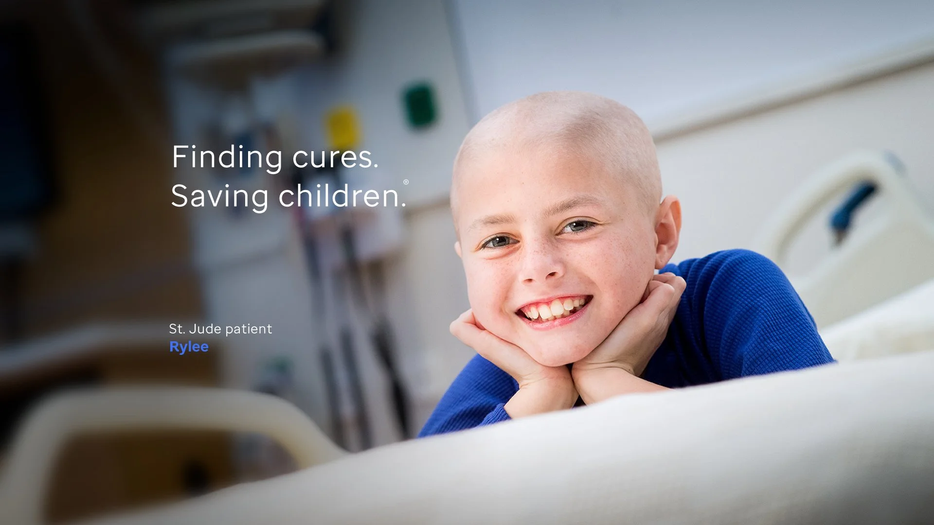 Smiling young boy in hospital bed with hands under chin in a hospital room.