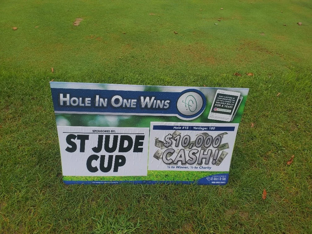 Sign on a golf course promoting a game where a hole in one wins $10,000 cash, sponsored by St Jude Cup, with instructions to pose a picture of your golf ball for a chance to win for a year.