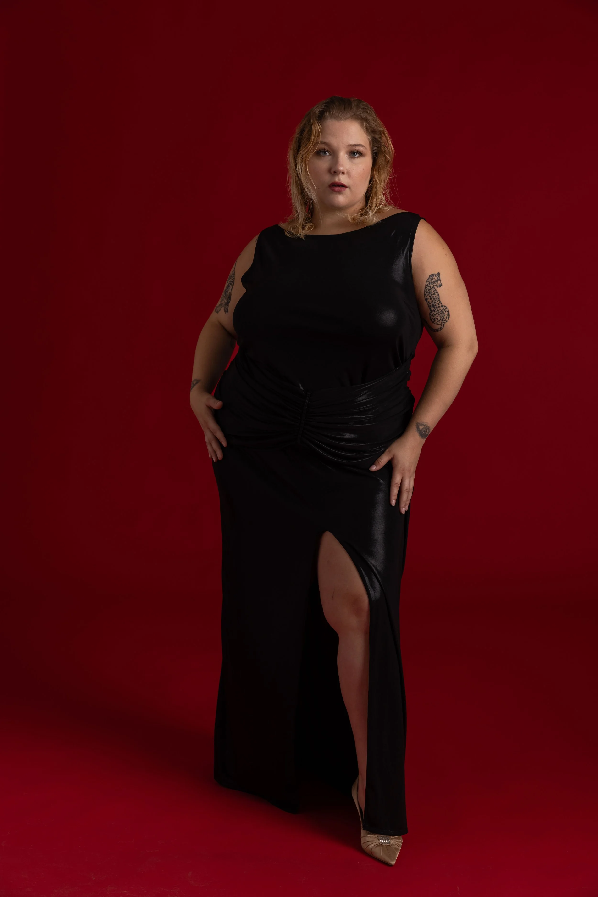 Femme portant une robe noire avec une fente, debout devant un fond rouge.