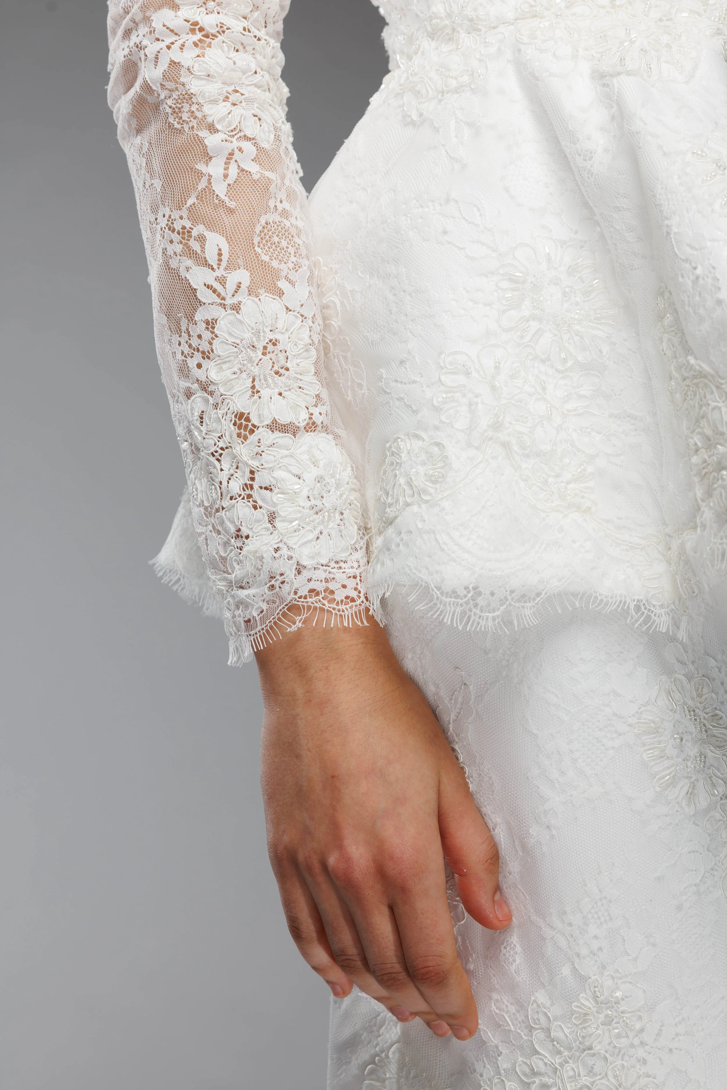 Main d'une femme posant à côté d'une robe de mariée en dentelle blanche avec des motifs floraux.