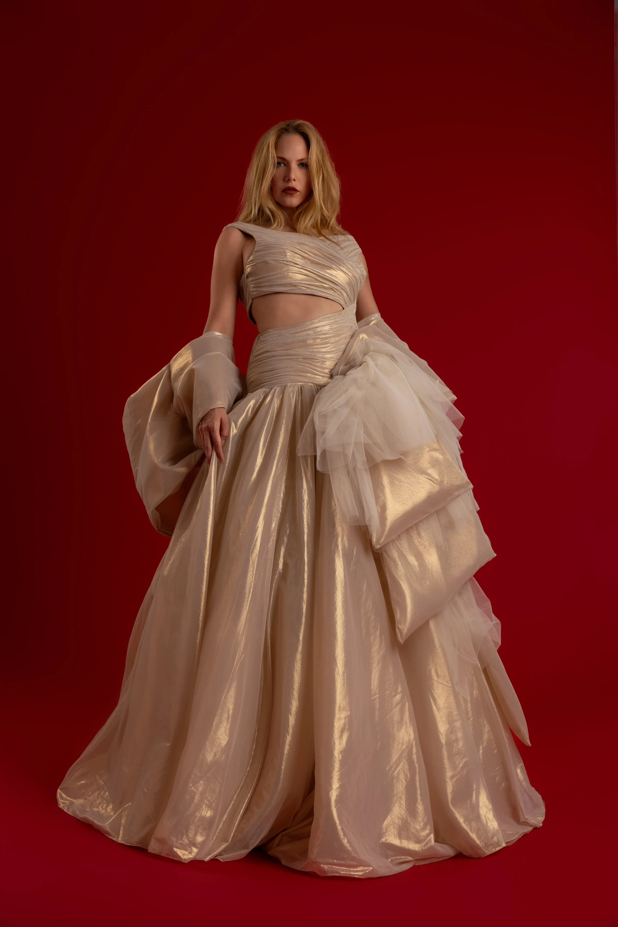 Femme portant une robe de soirée en satin beige avec un haut court et une jupe ample, accentuée par un fond rouge