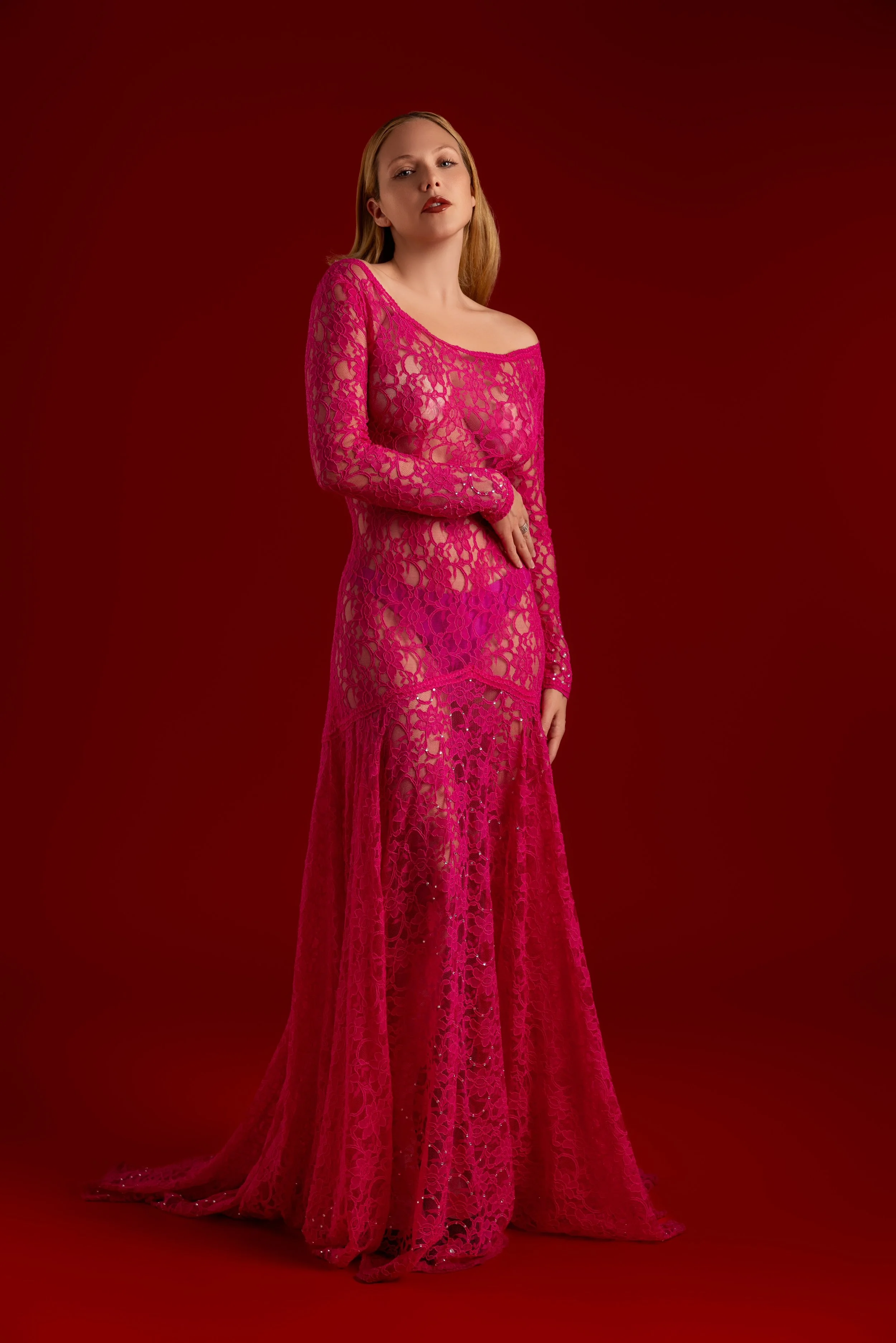 Une femme portant une robe longue en dentelle rose sur fond rouge.