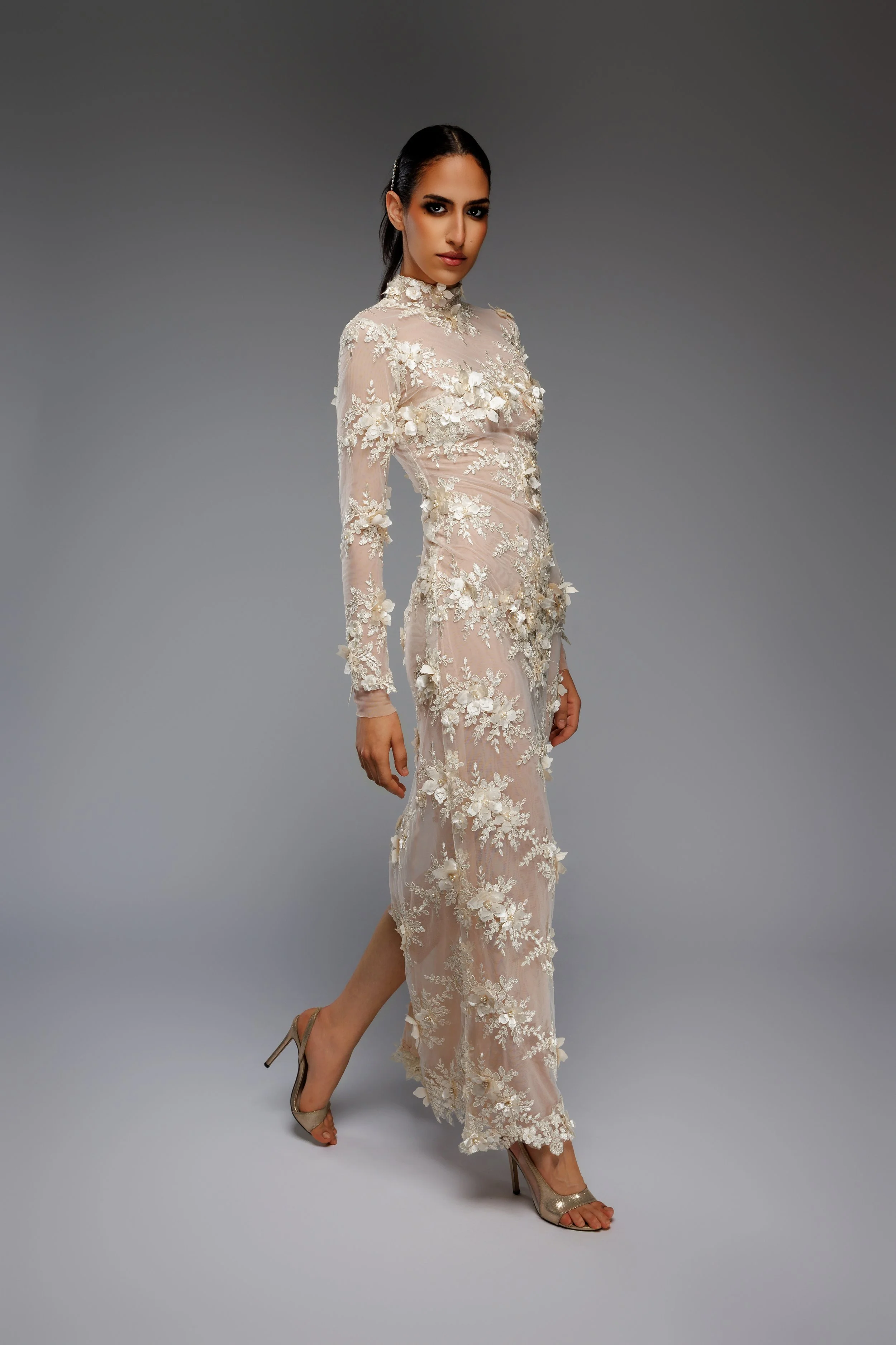 Femme en robe de mariage élégante en dentelle fleurie avec des talons dorés sur un fond gris