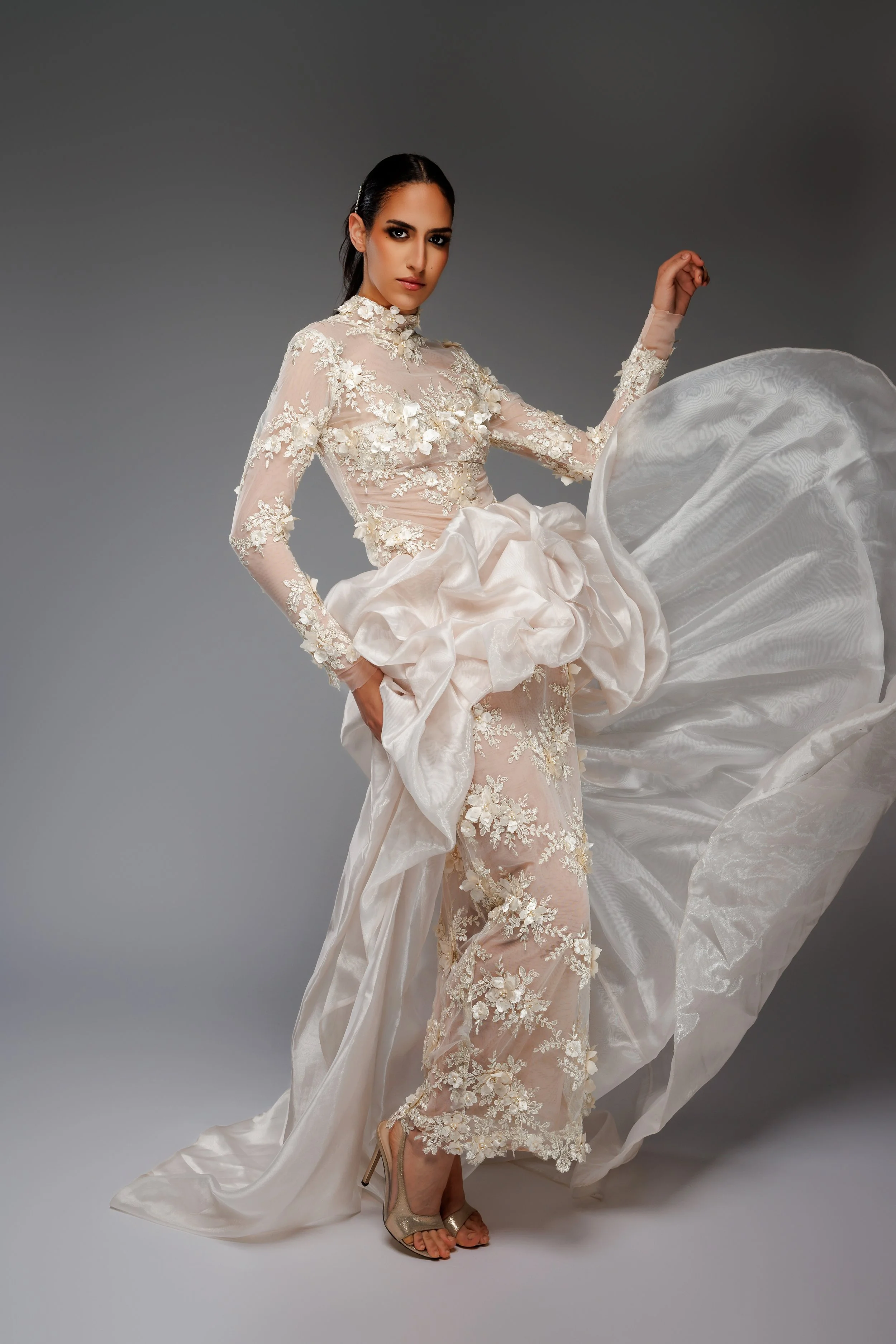 Femme portant une robe de mariée élégante avec des détails en dentelle et un jupon volumineux en satin, posant contre un fond gris.