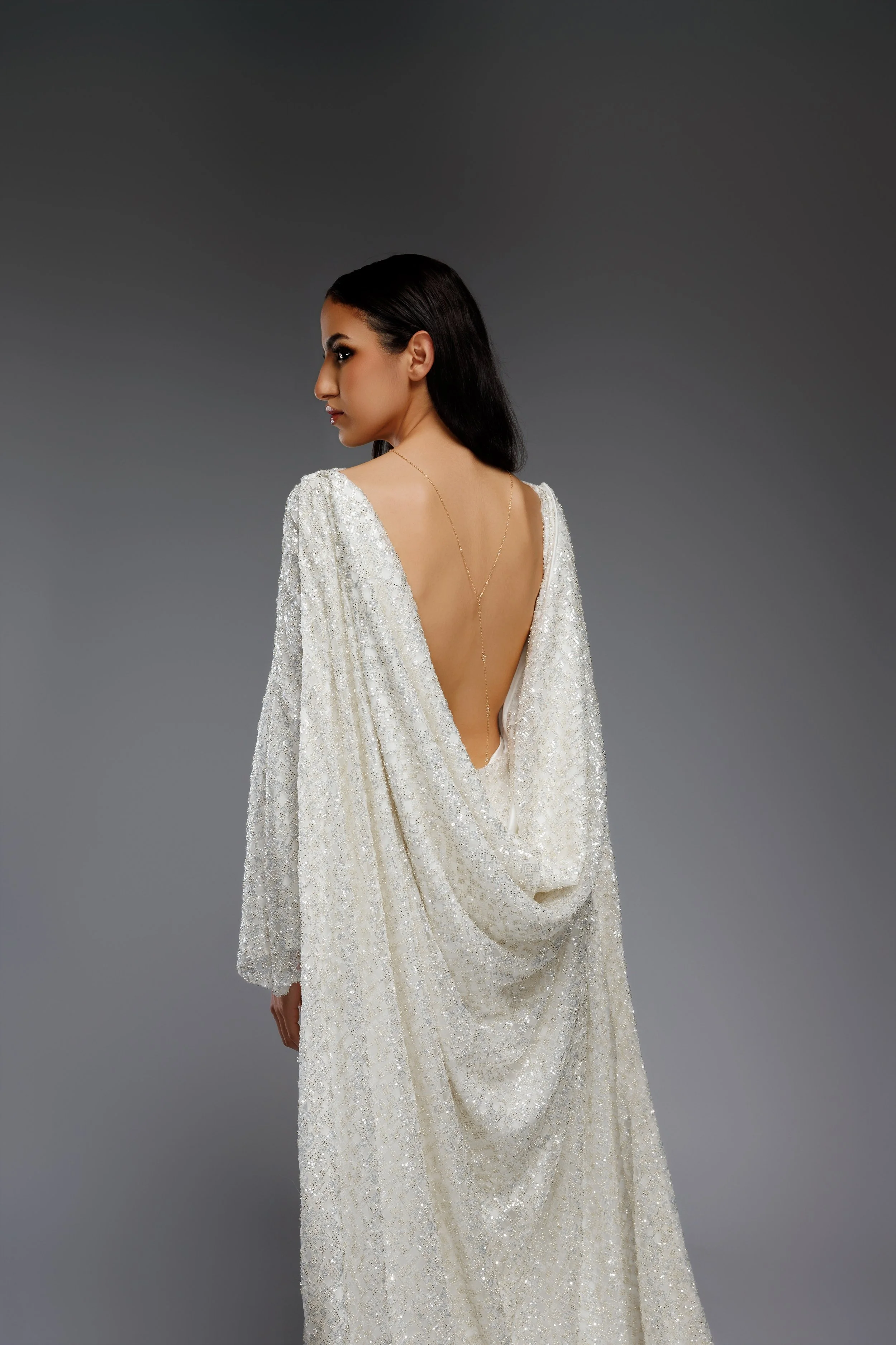 Femme portant une robe de soirée blanche avec un décolleté dans le dos, cheveux noirs, fond gris