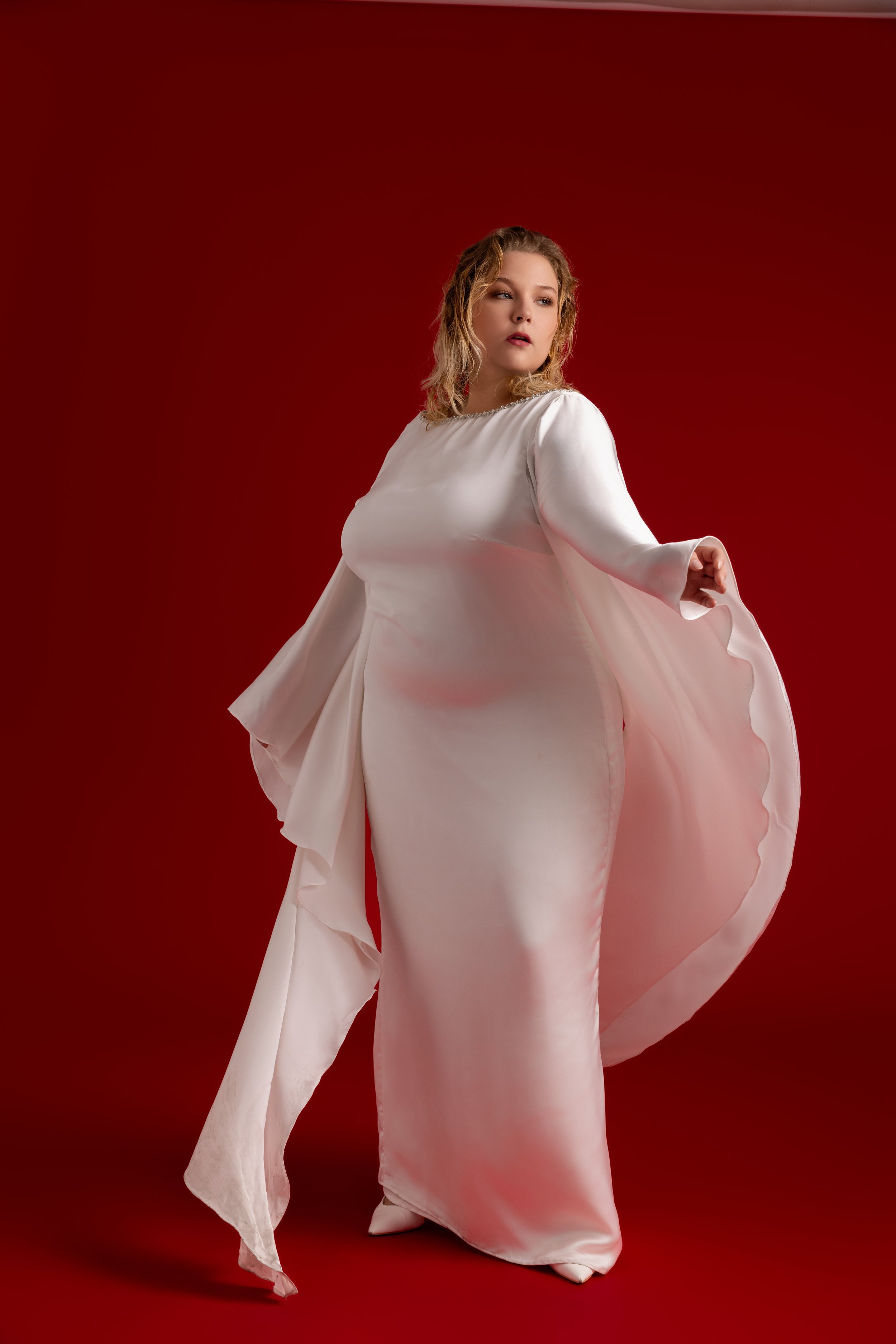 Femme en robe de soirée blanche dans un studio avec fond rouge