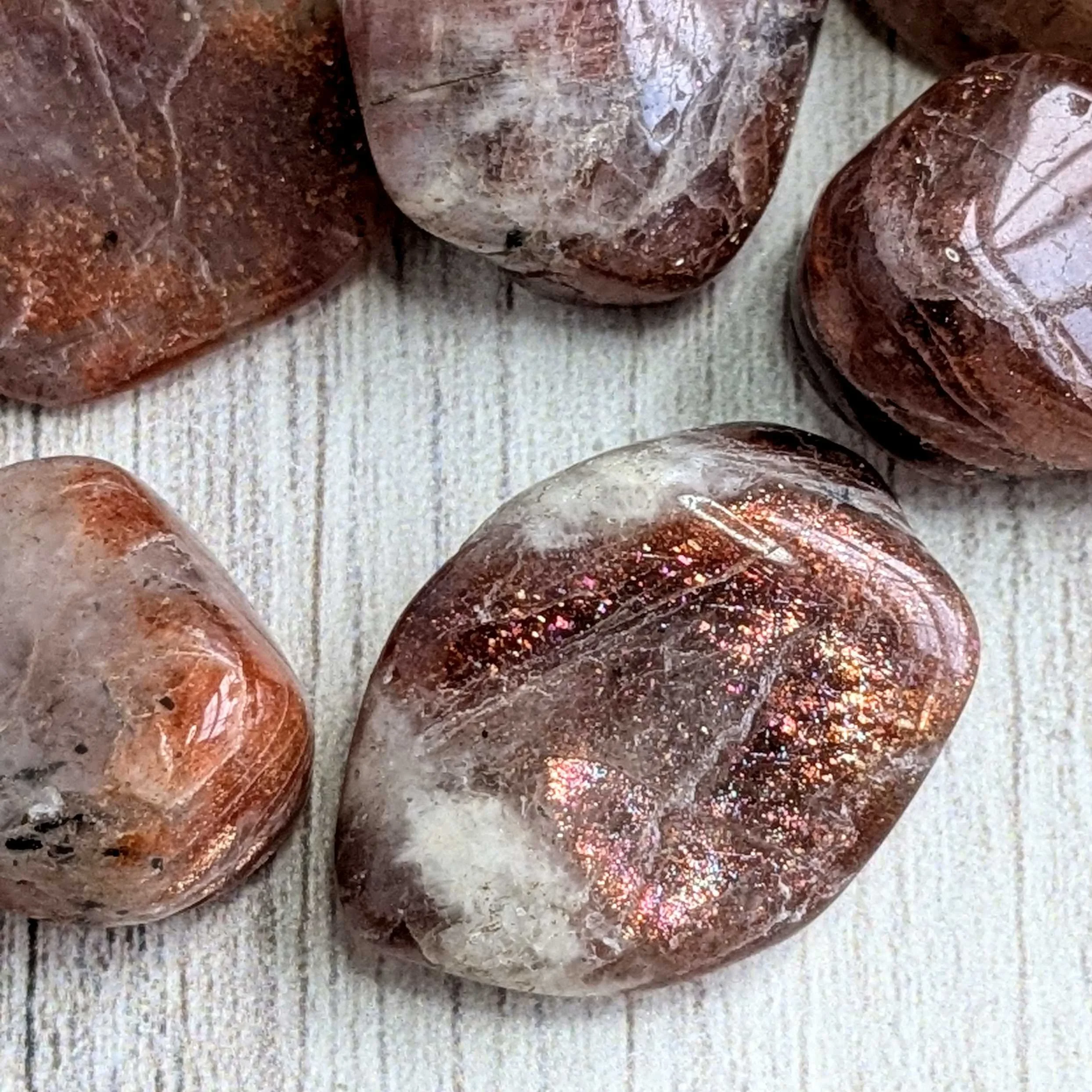 A close-up of several polished stones with reddish-brown, white, and iridescent colors on a white textured wooden surface.
