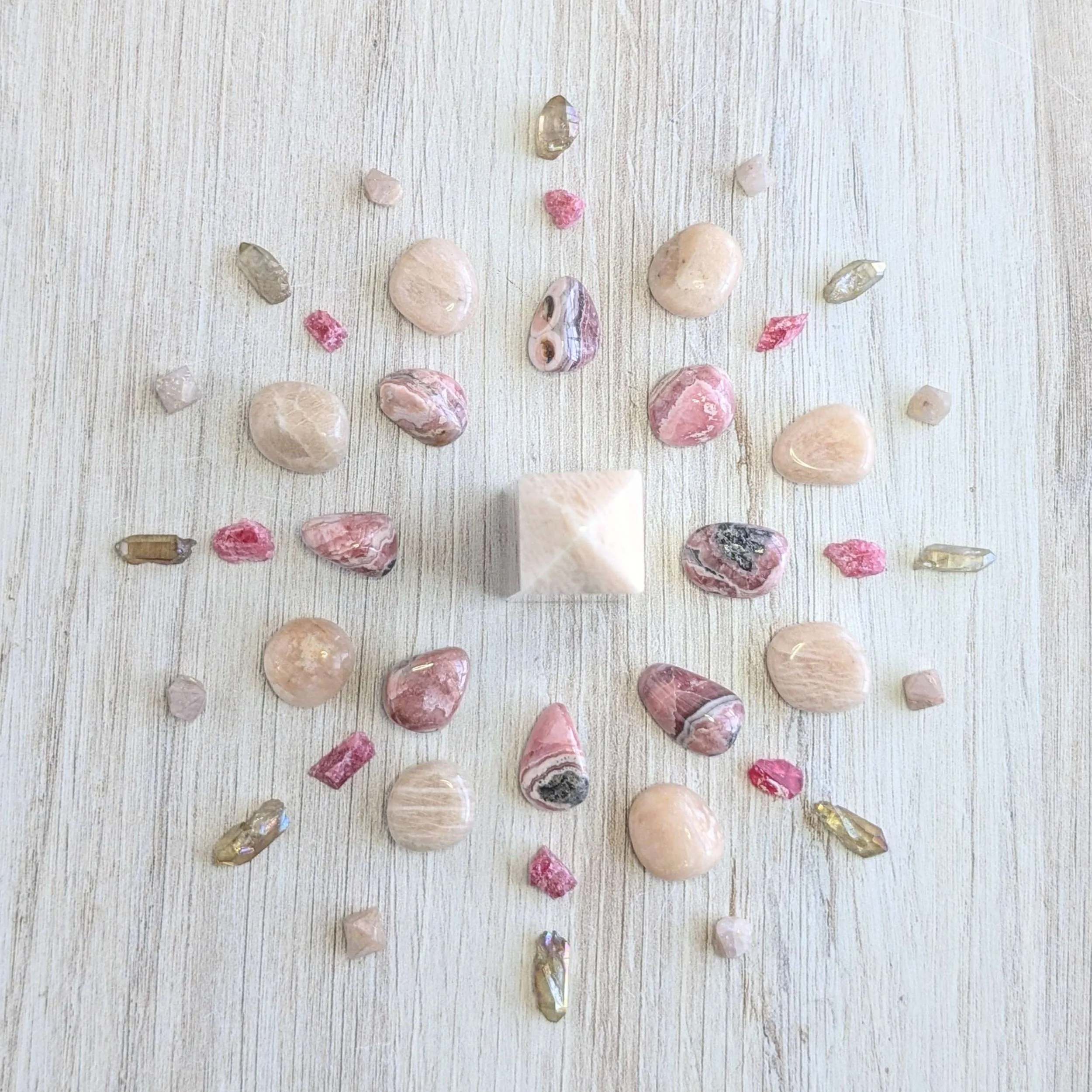 Arrangement of pink, beige, and clear gemstones surrounding a Cream Moonstone tower on a light wooden surface.