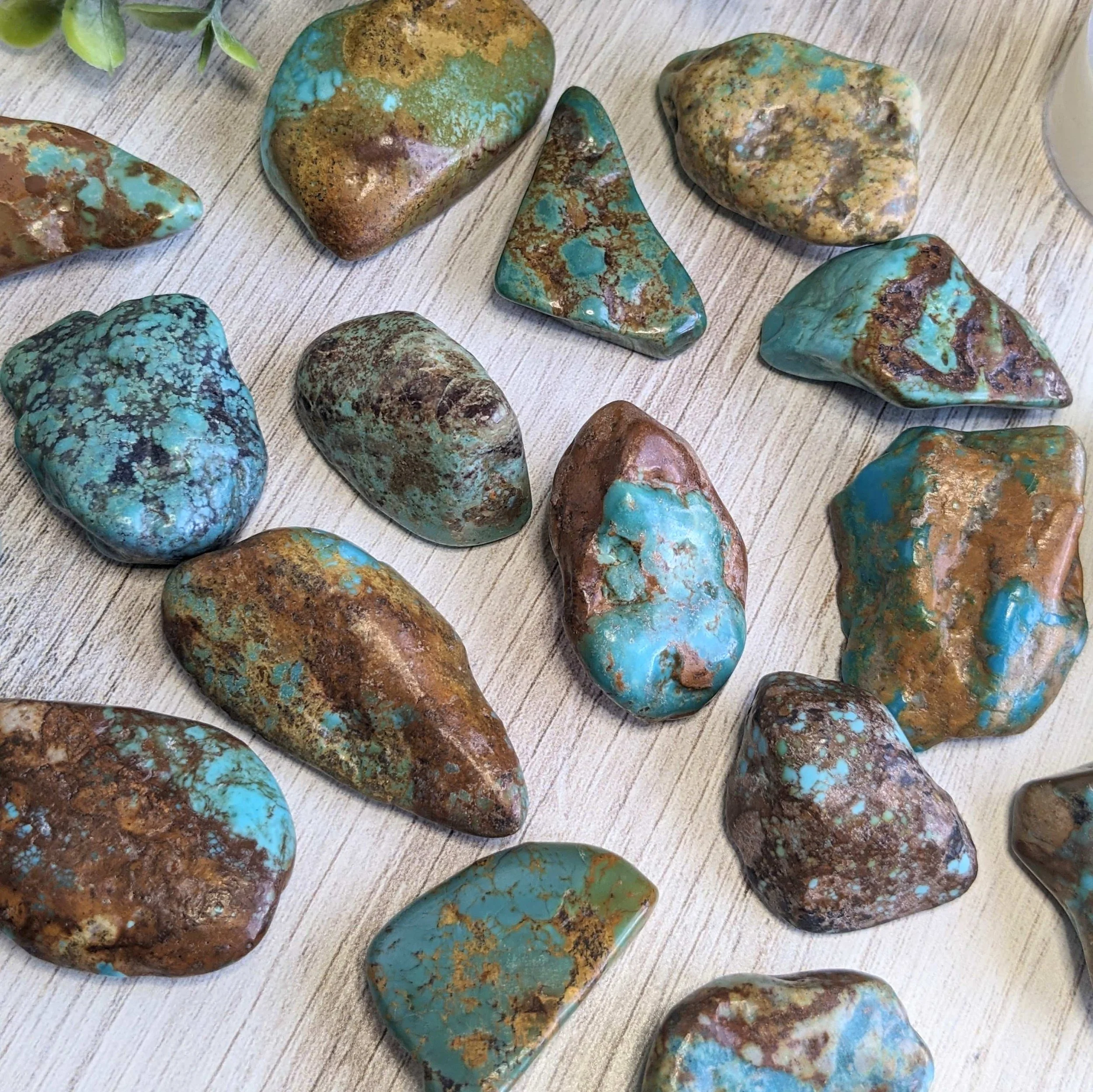 Collection of tumbled turquoise stones with brown and green matrix patterns on a wooden surface.