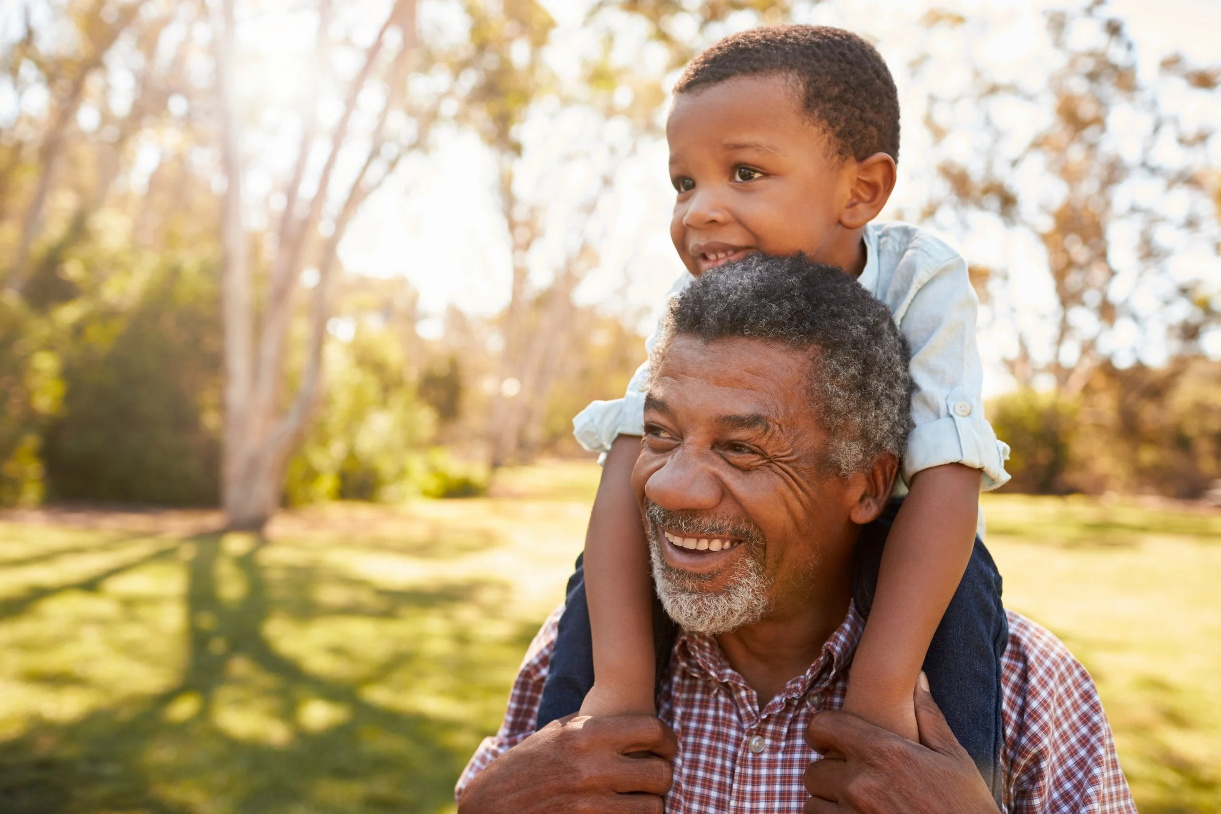 A grandfather able to communicate better with his grandson while his grandson rides on his shoulders during an outdoor walk. The grandfather receives cognitive-communication therapy after TBI in Edmond, OK.