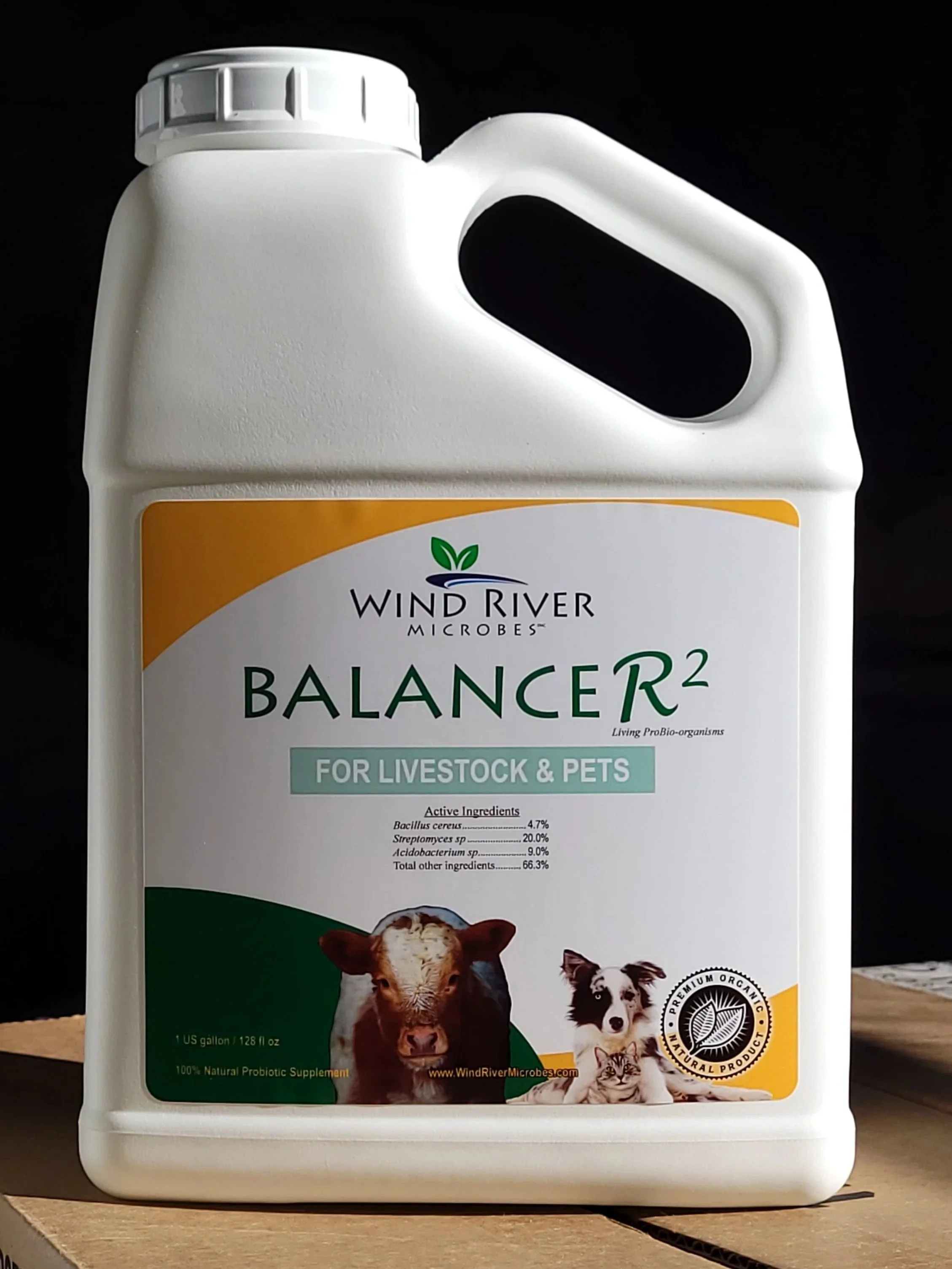 A white jug of Wind River Microbes Balance R2 probiotic supplement for livestock and pets with a label showing a cow, a dog, and a cat, and text indicating it contains active ingredients like Bacillus cereus, Streptomyces sp., and Acido bacterium sp.