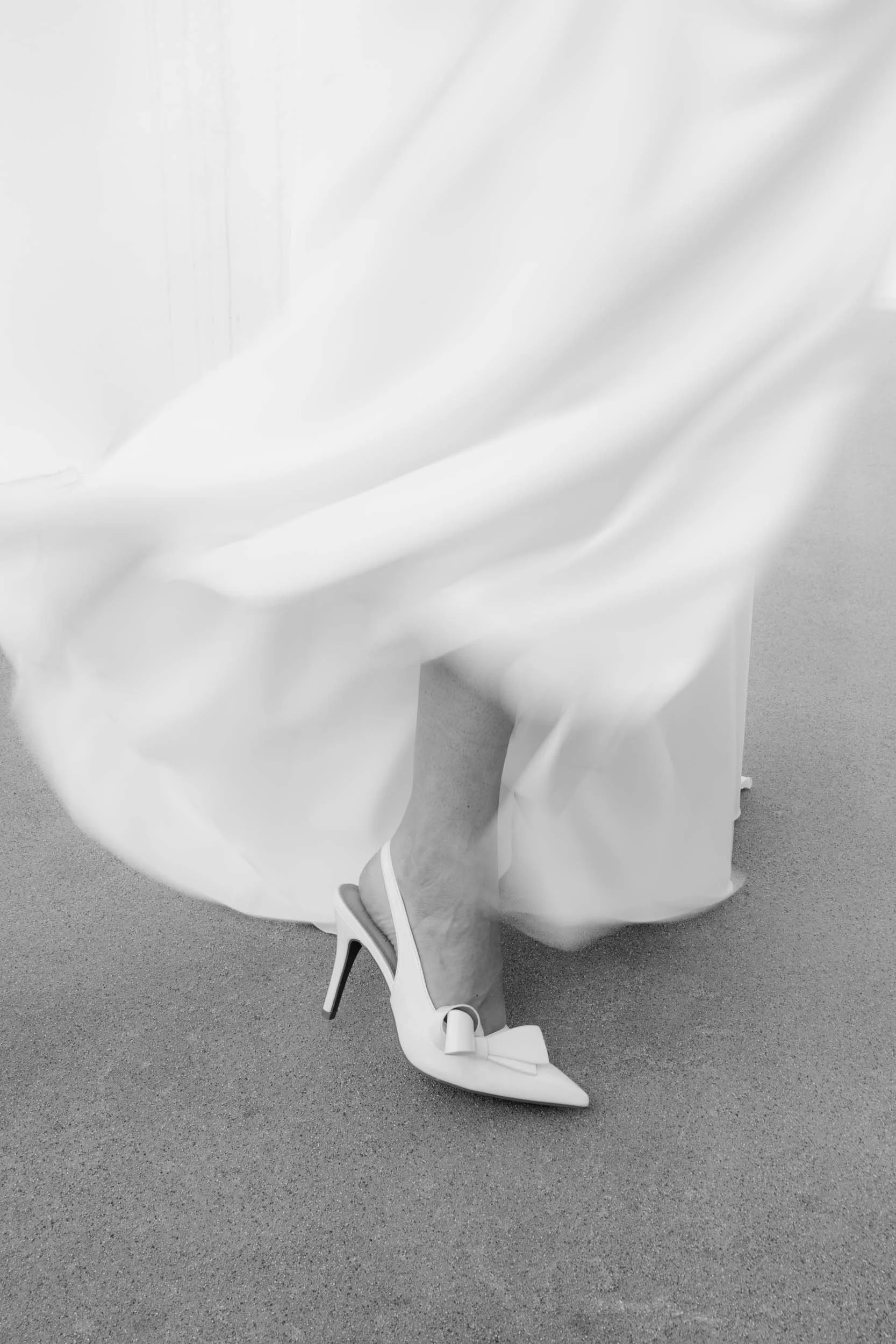 Dokumentarische Hochzeitsfotografie Hamburg: künstlerische Detailaufnahme vom Brautschuh und fließendem Kleid in Schwarz-weiß. Editorial-Ästhetik für anspruchsvolle Paare von Valeska Weddings.