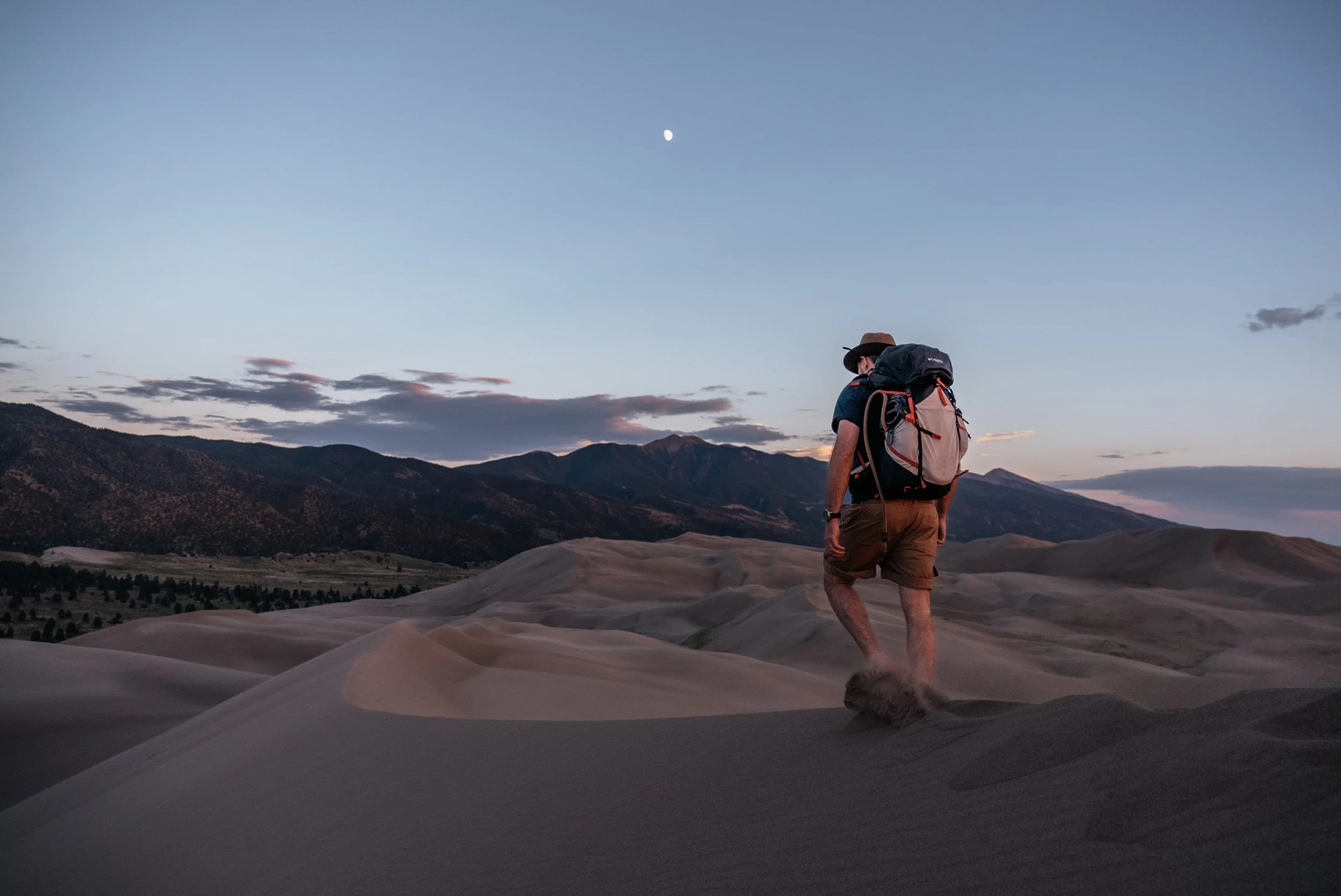 man hiking on sand dunes at blue hour