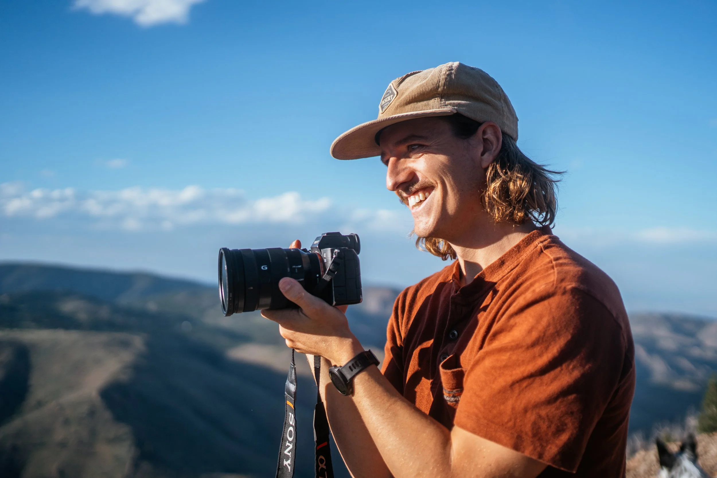 Roo smith holding a camera in the sunshine in the mountains