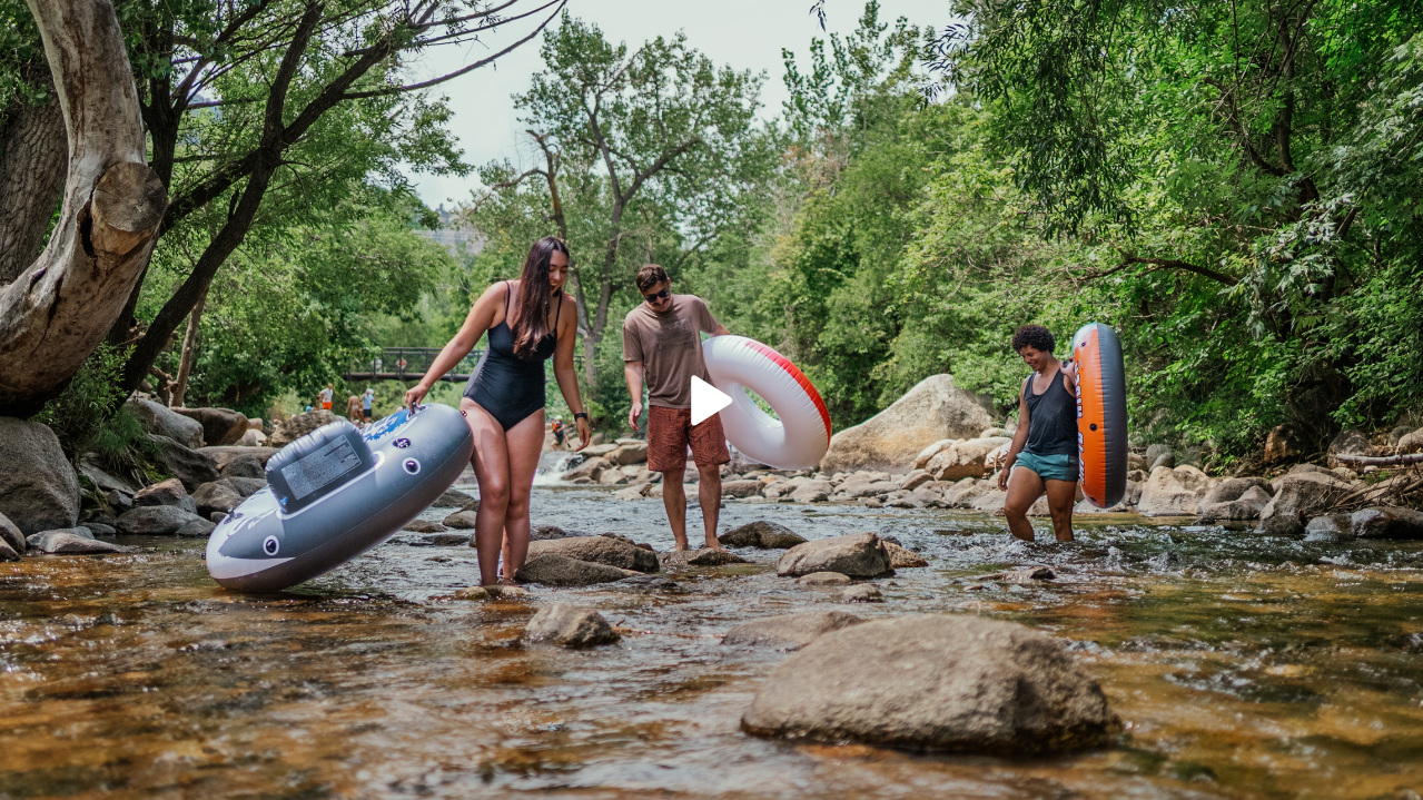 three people walking with inner tubes in Boulder creek for a photoshoot
