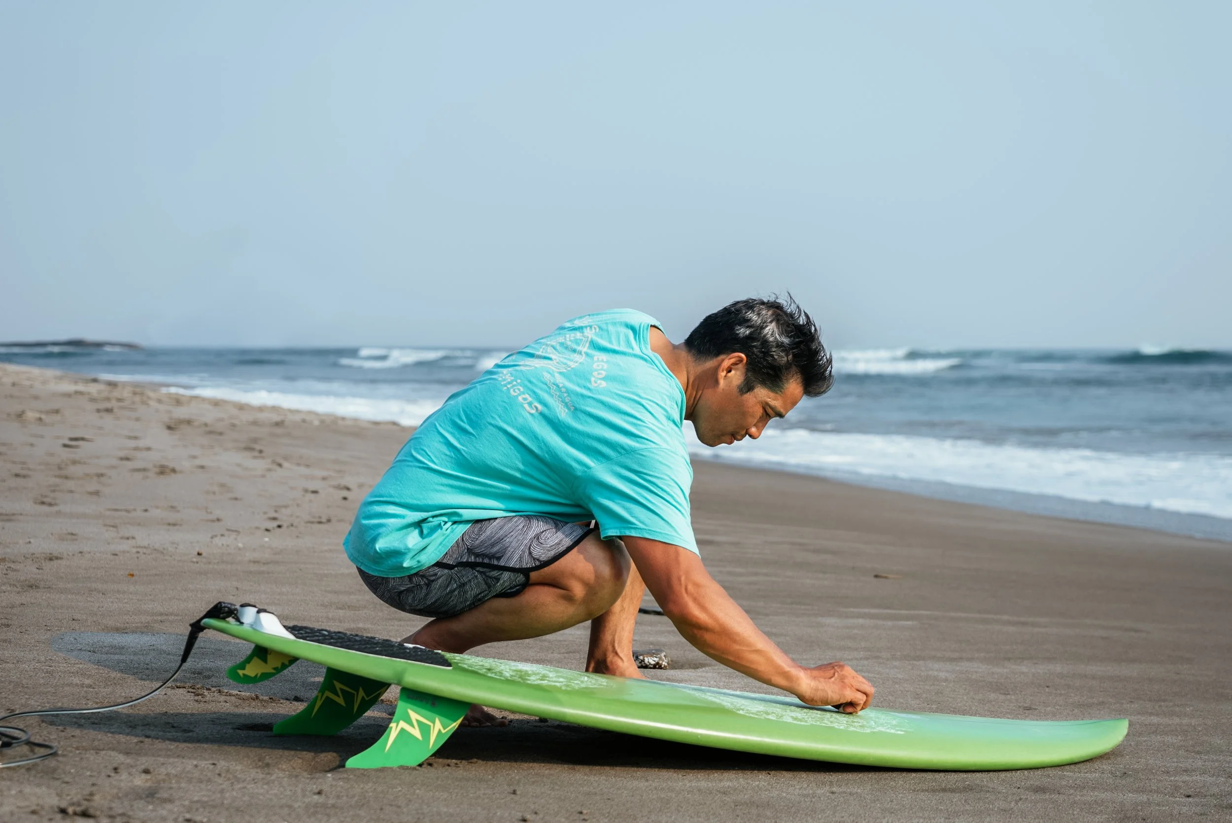 man waxing a green surfboard before going in the water