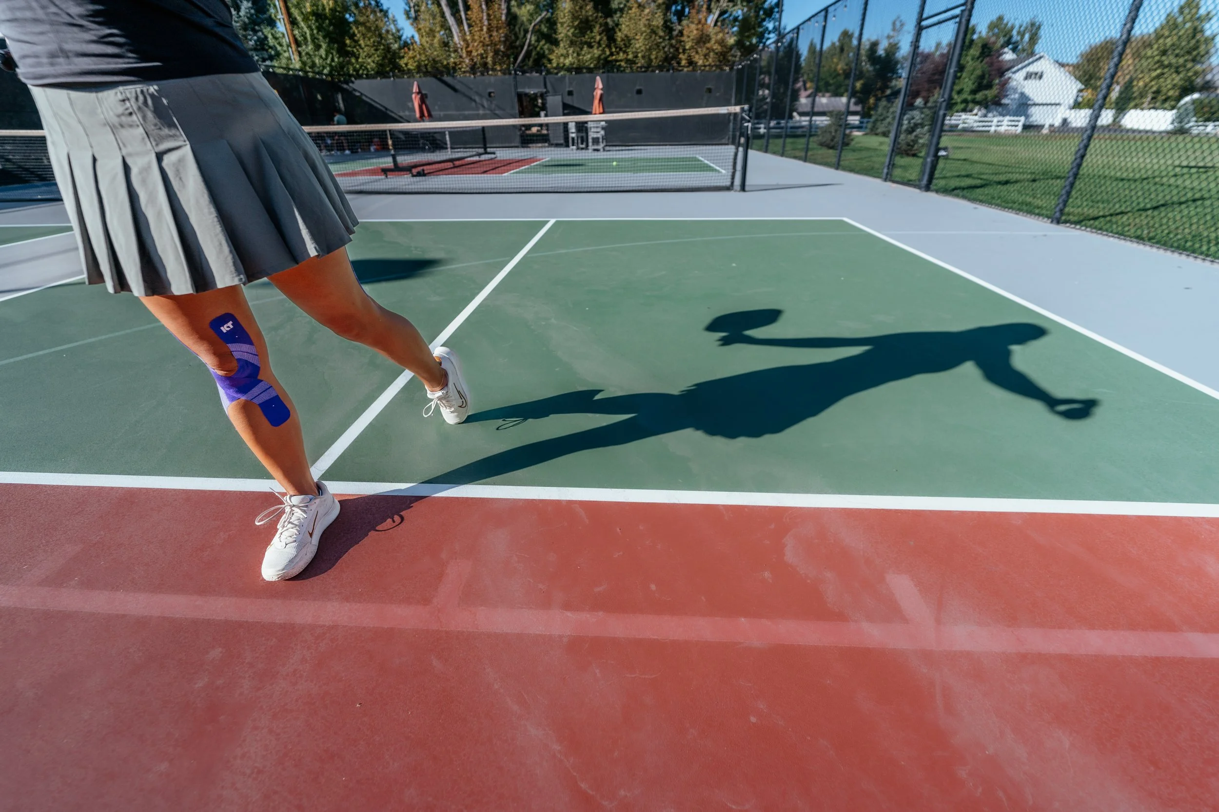 women in a skirt with KT Tape on her knee playing pickleball