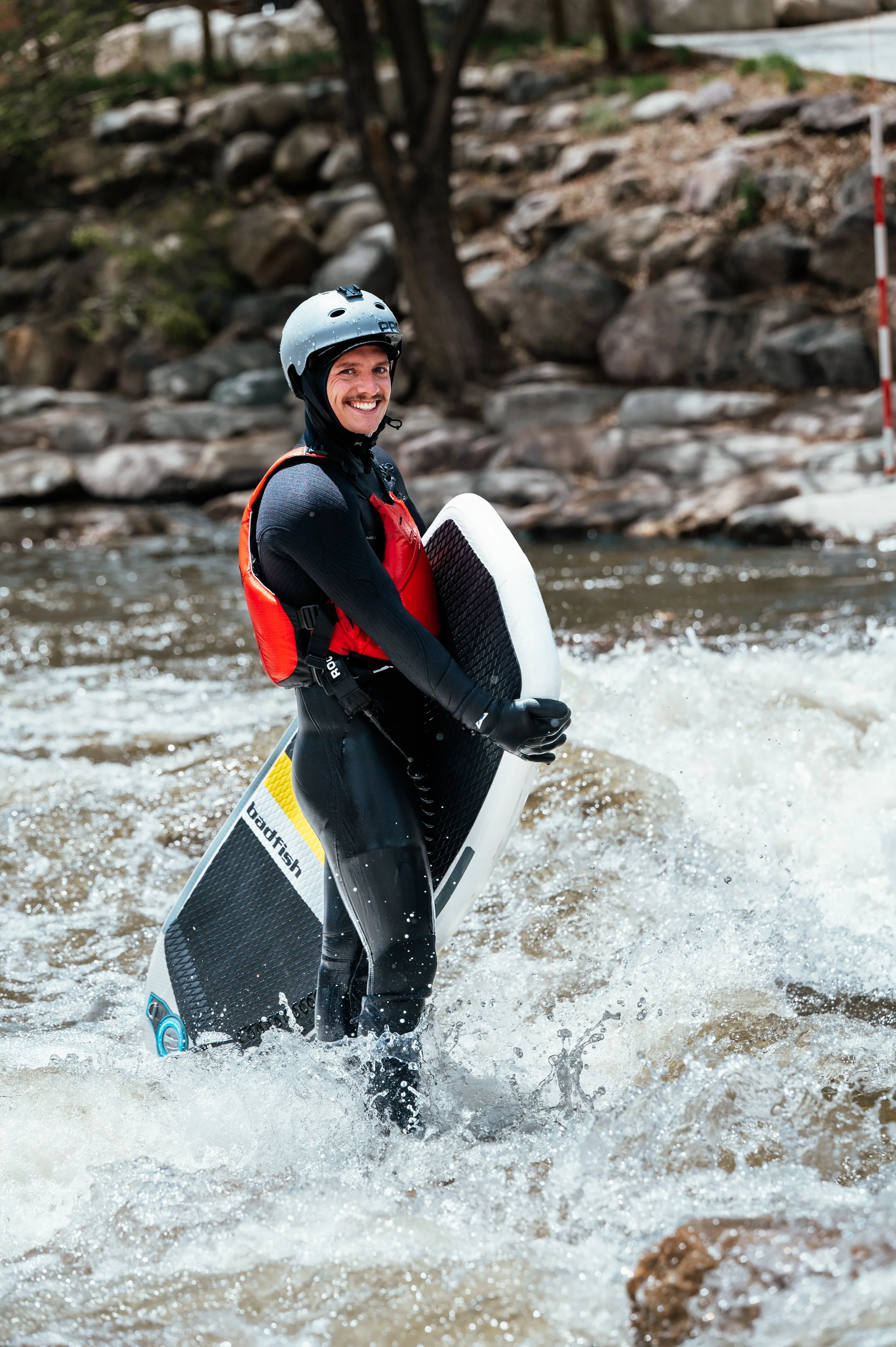 Roo Smith smiling at the camera while ankle deep in the river waiting to surf