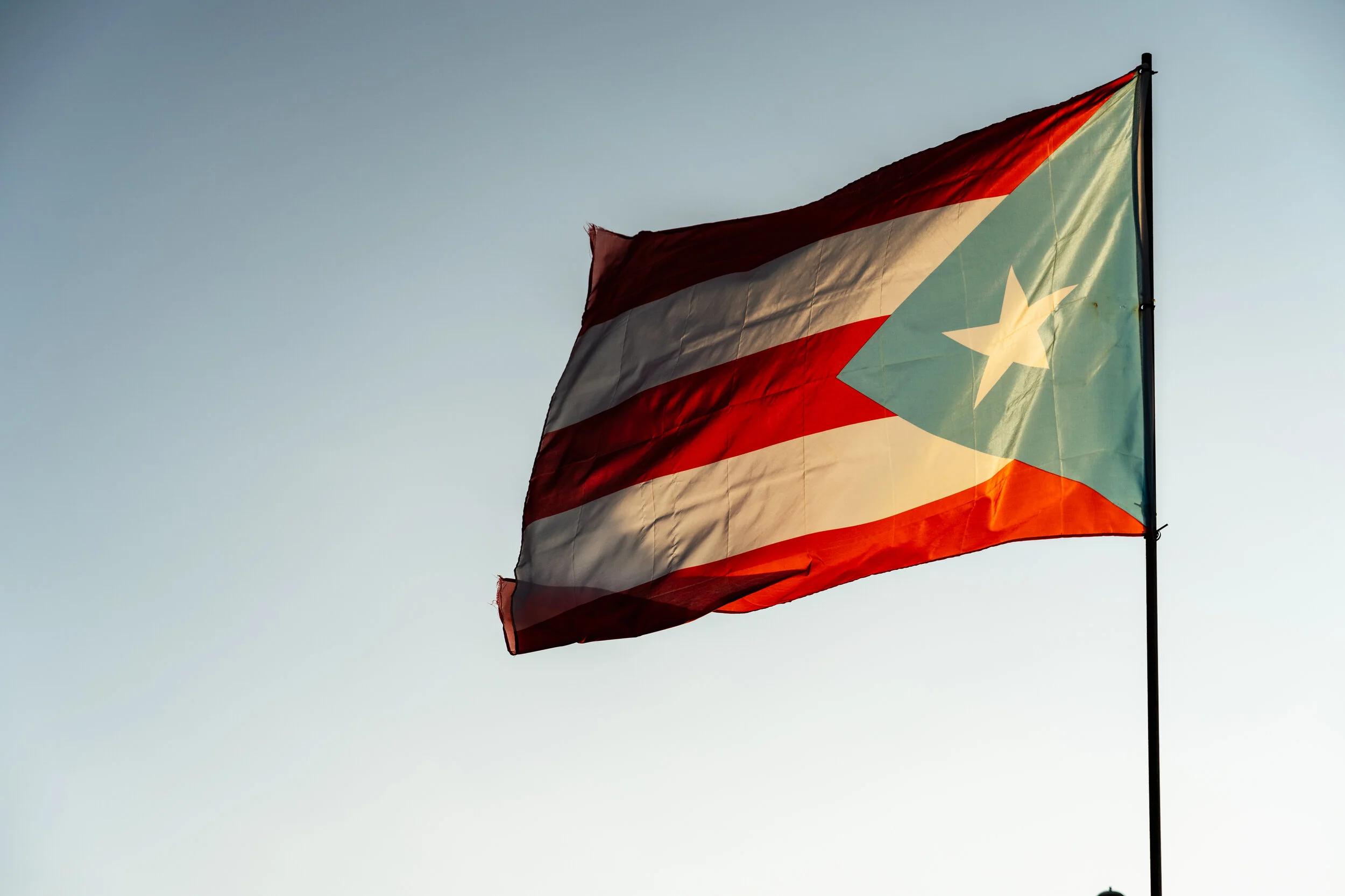 Puerto Rican flag flying in the wind against a clear sky.