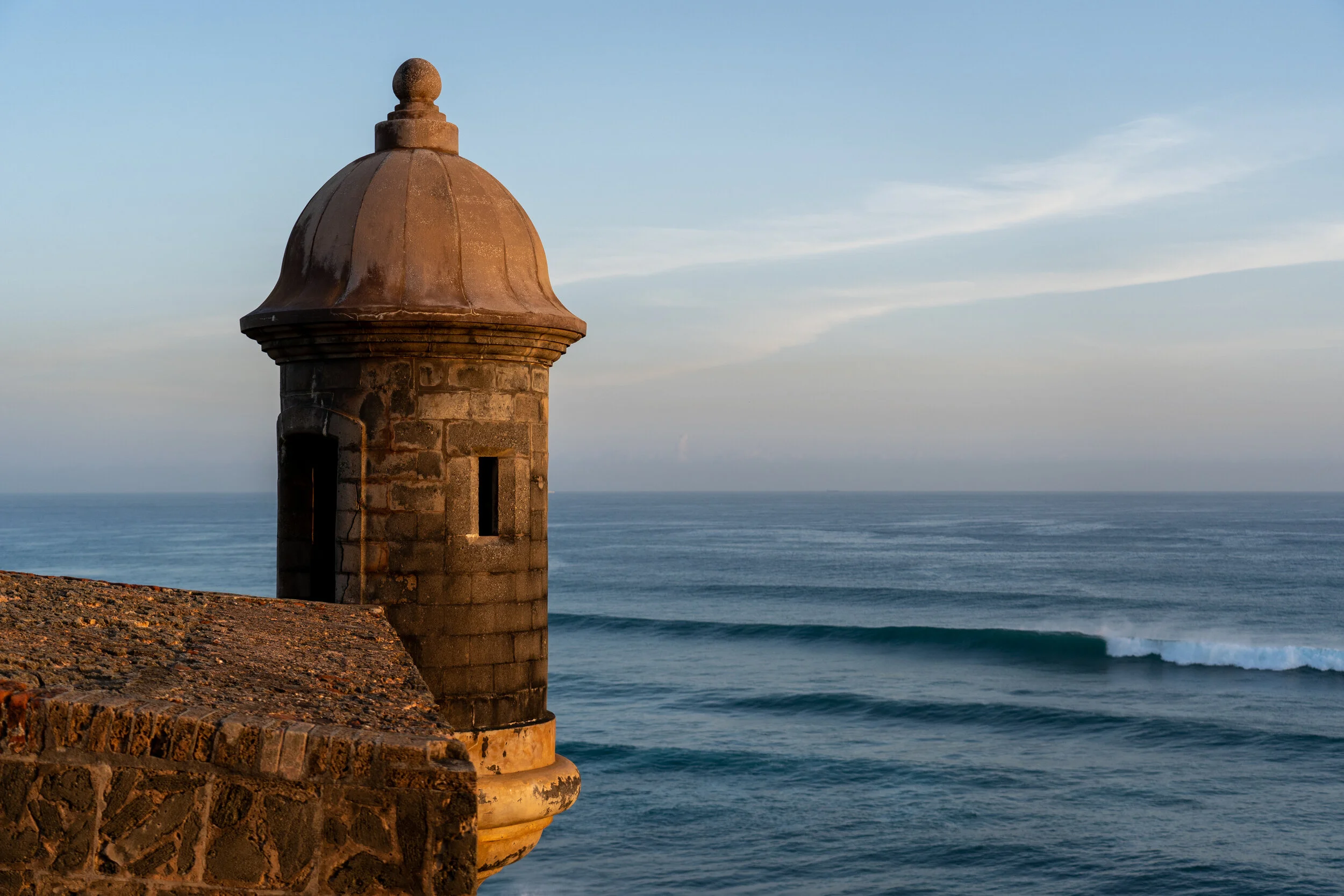 A small stone lighthouse on a seaside cliff overlooking the ocean on a clear day.