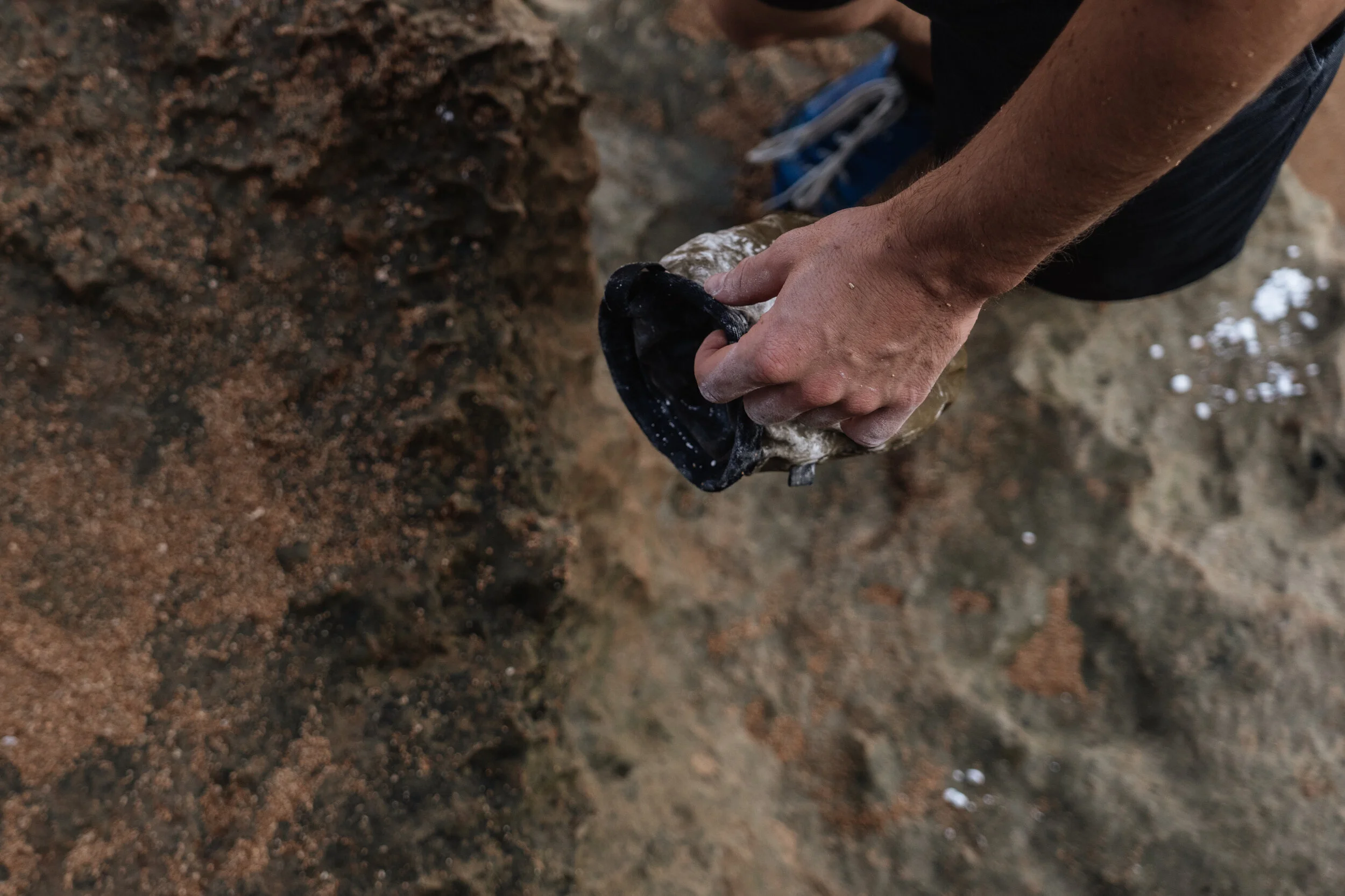Person using a black and gray shovel to dig in sandy soil.