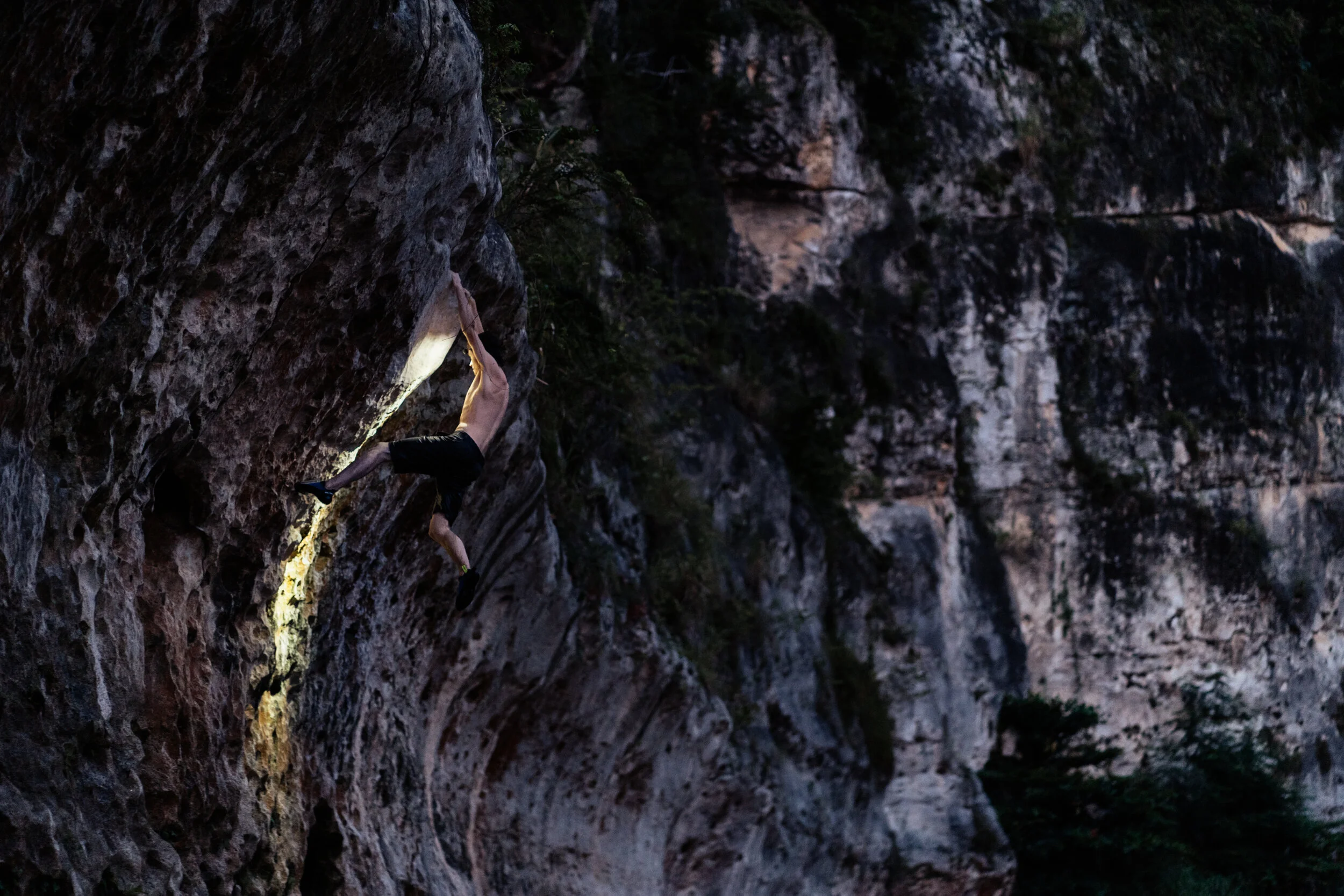 A person rock climbing on a vertical stone cliff during dusk or nighttime.
