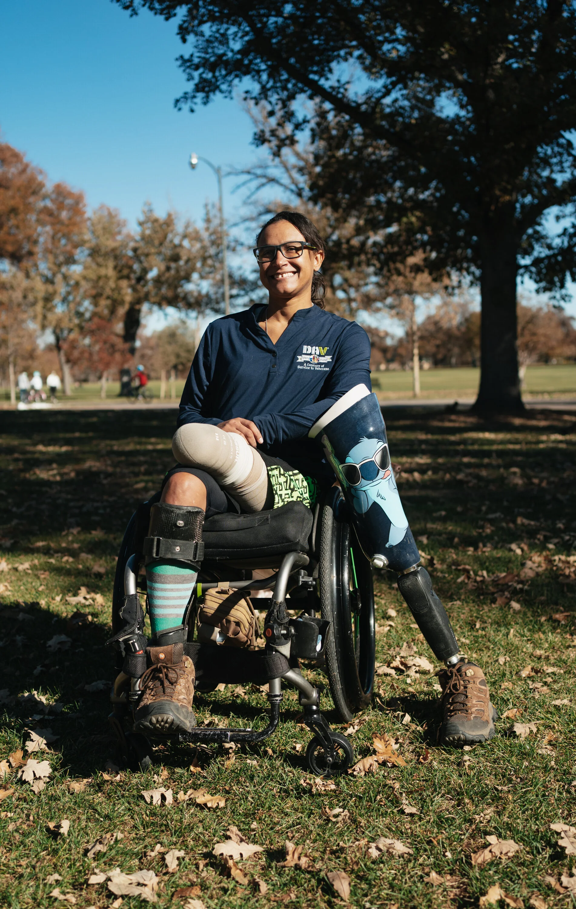 A woman in a wheelchair smiling at a park with trees and blue sky