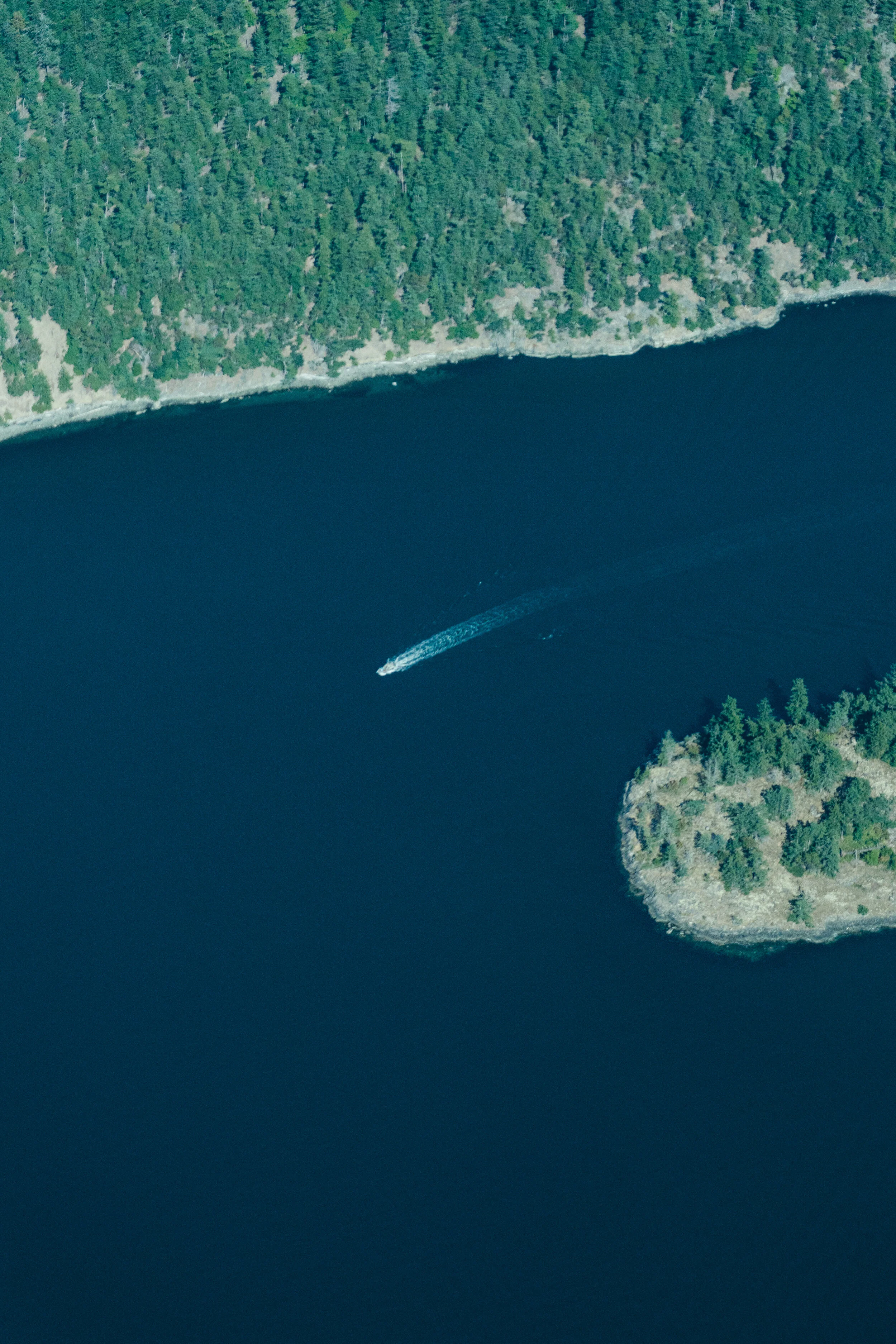 Aerial view of a boat sailing on a dark blue lake surrounded by dense green forest.