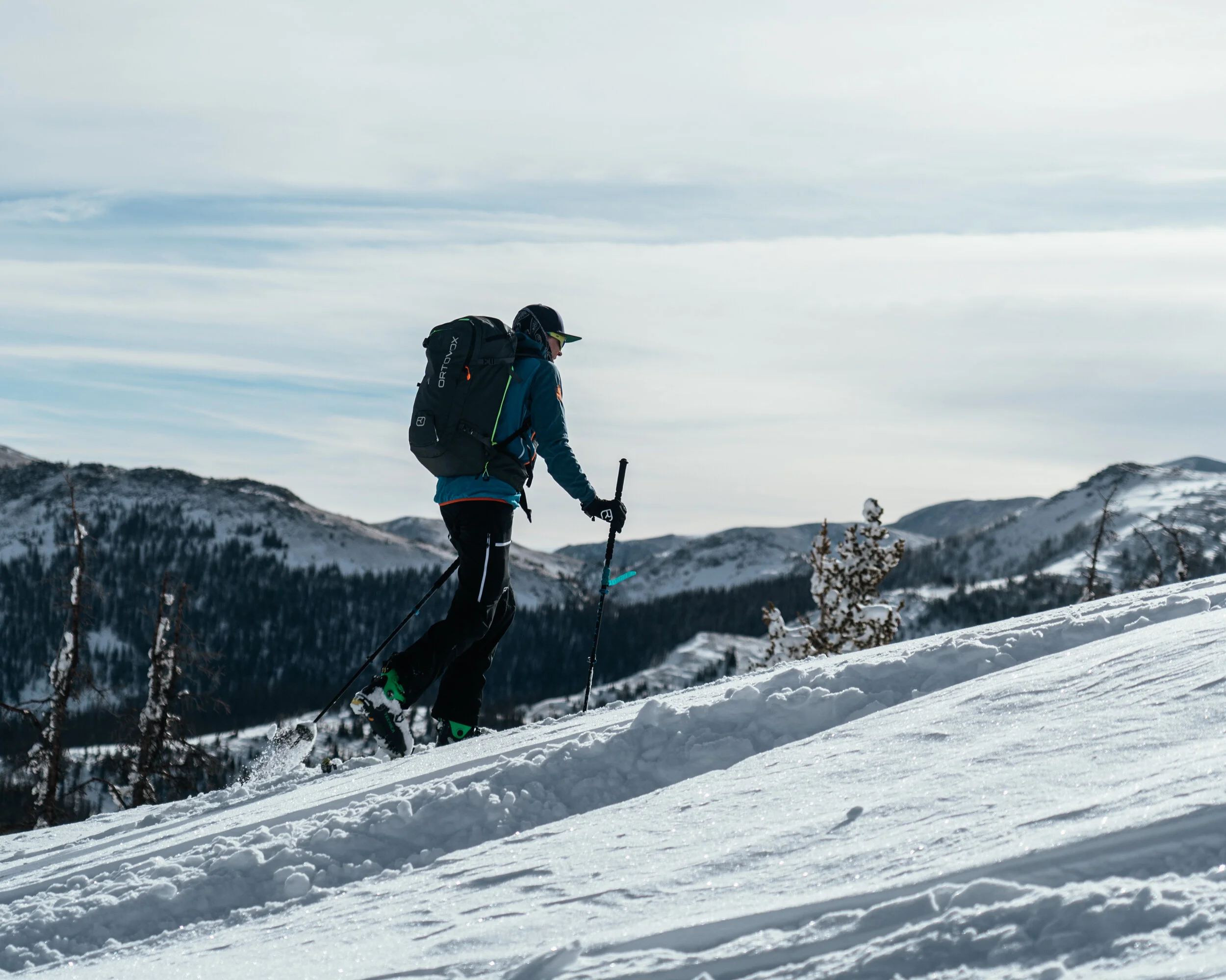 A person wearing winter gear, including a backpack and gloves, skiing uphill in a snow-covered mountain landscape during daytime.