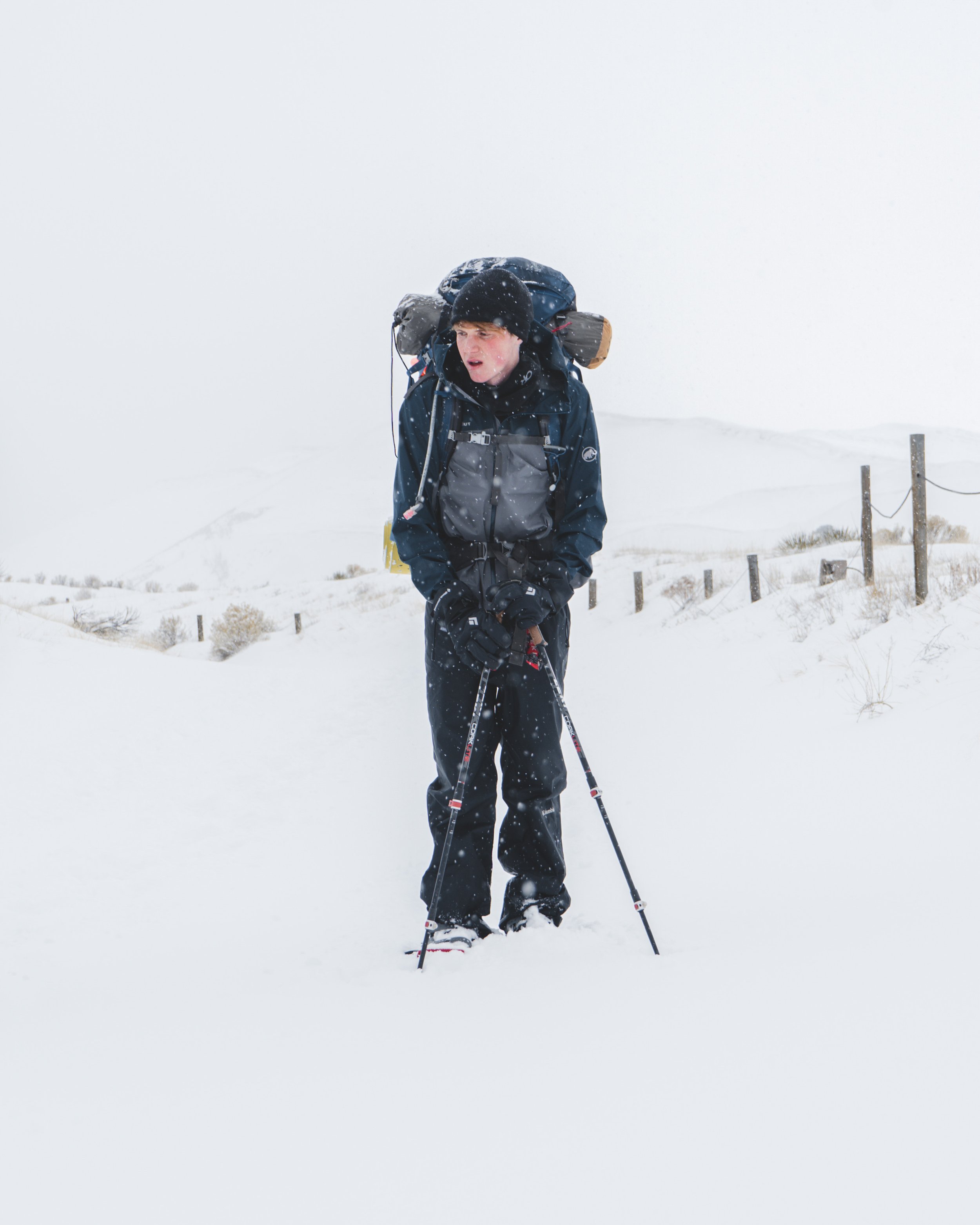 A person hiking in snowy weather, wearing outdoor gear and using trekking poles.