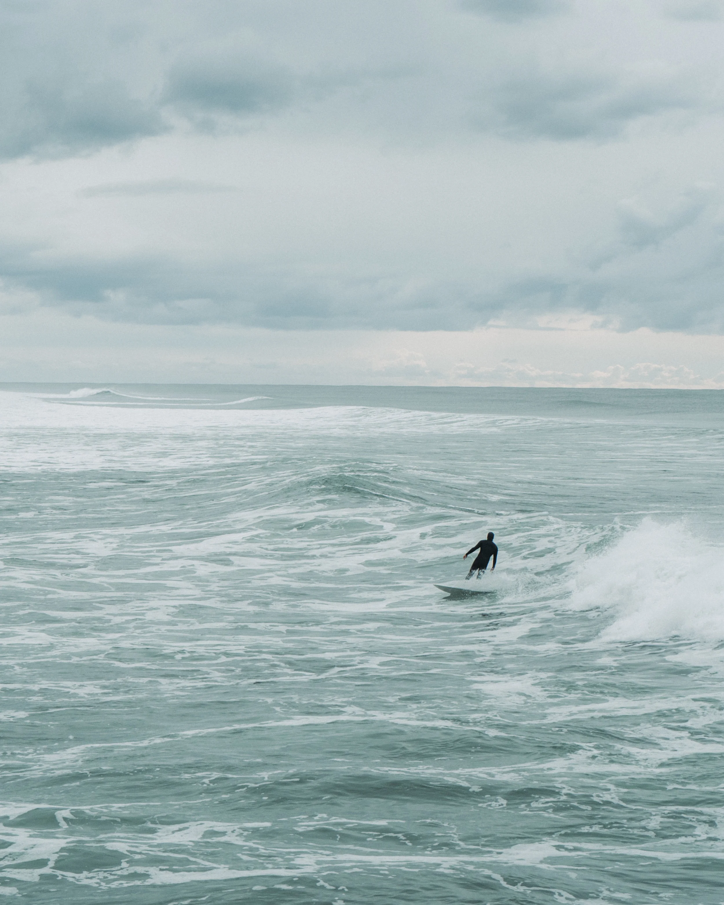 A person surfing on a wave in the ocean on a cloudy day.