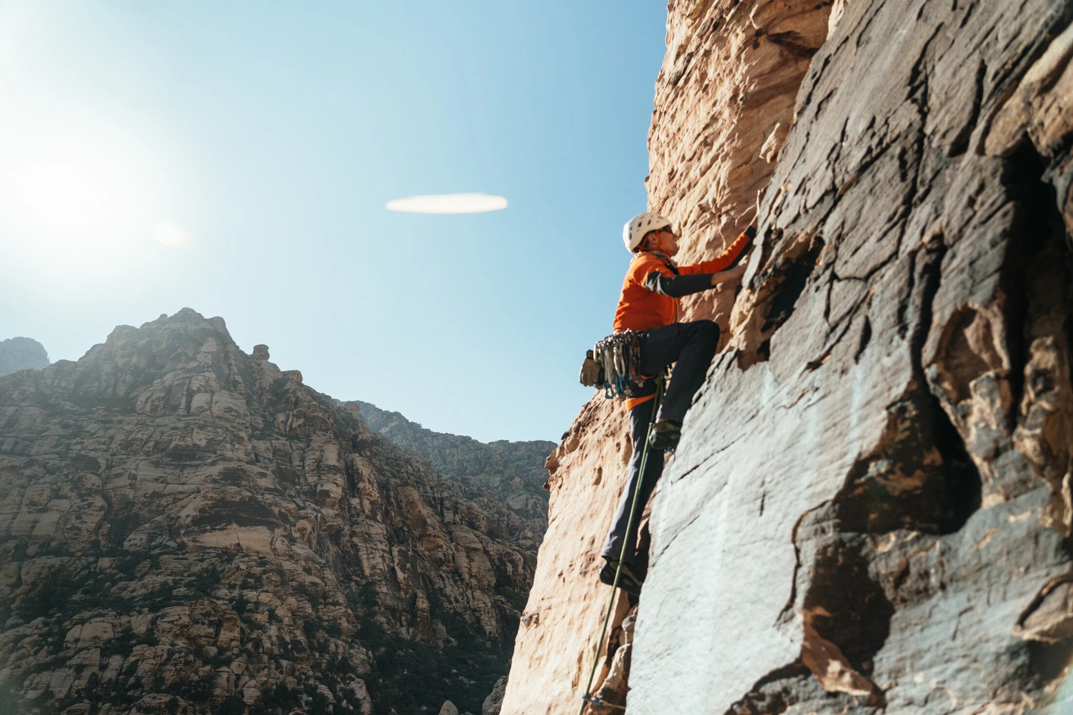 A person rock climbing on a steep cliff face in a mountainous area with blue sky in the background.