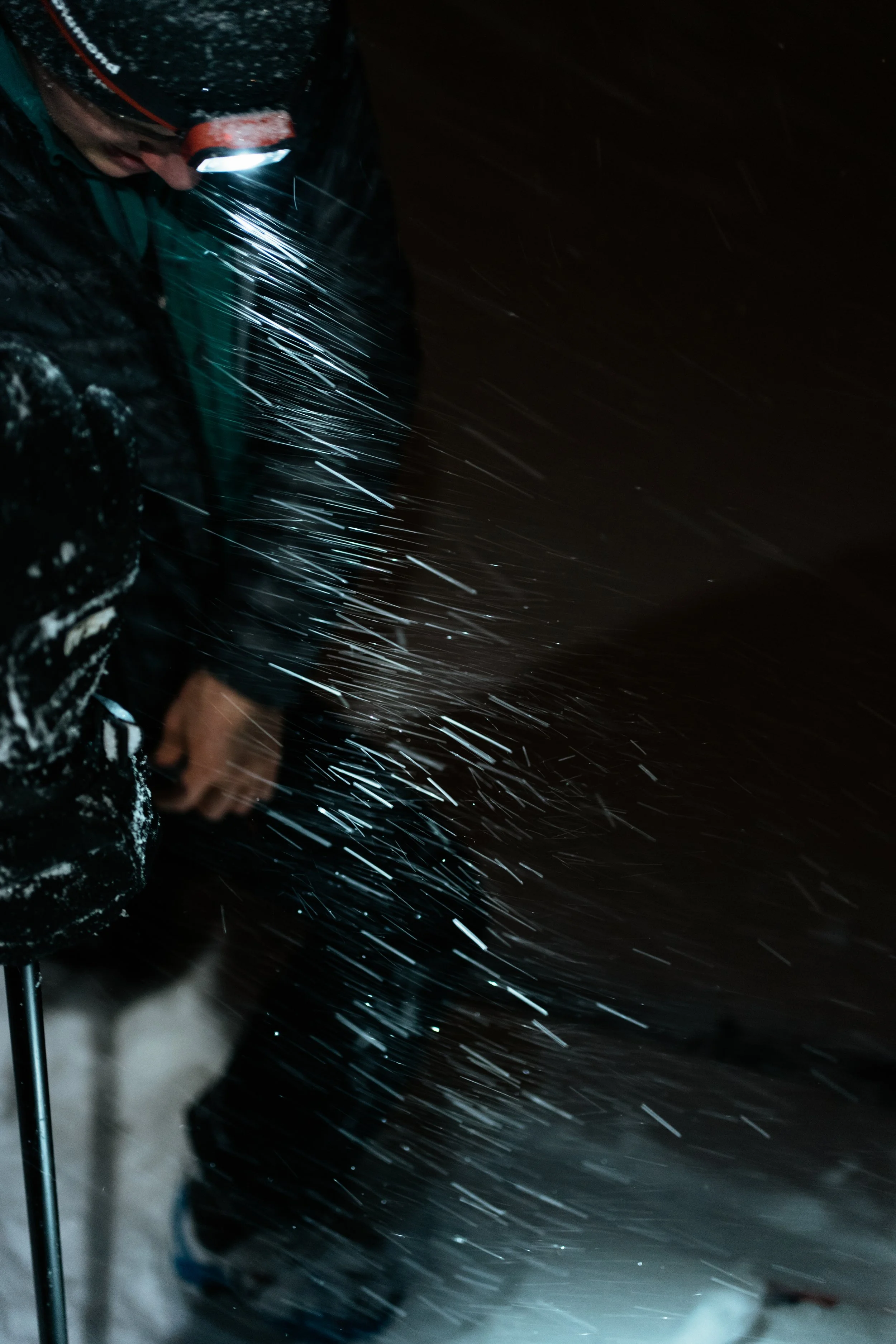 Person wearing winter gear and headlamp in a snowstorm at night