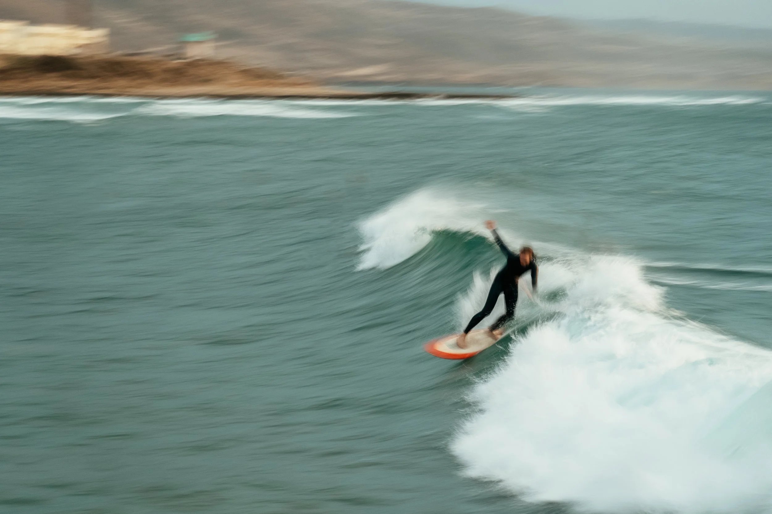A person surfing on a wave in the ocean near the coast.