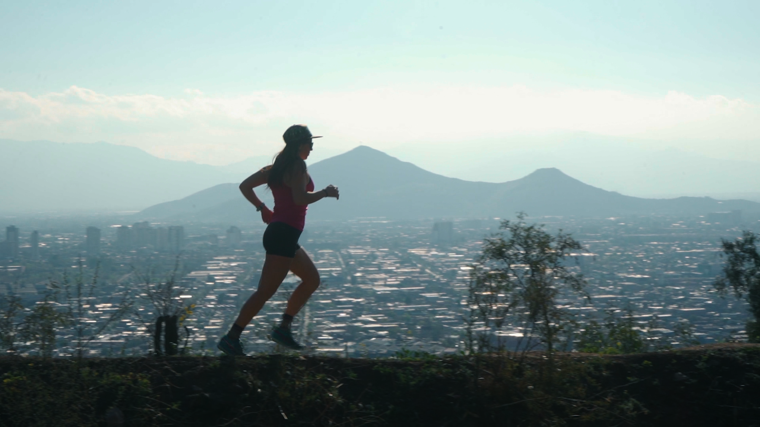 A woman jogging on a trail with a city and mountain range in the background.