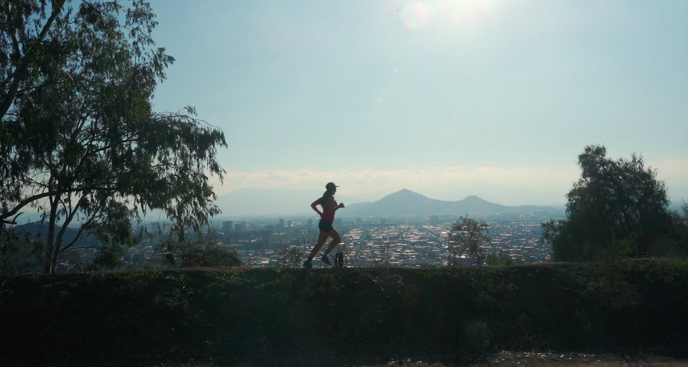 A woman running on a trail with a city skyline and mountains in the background during daytime.