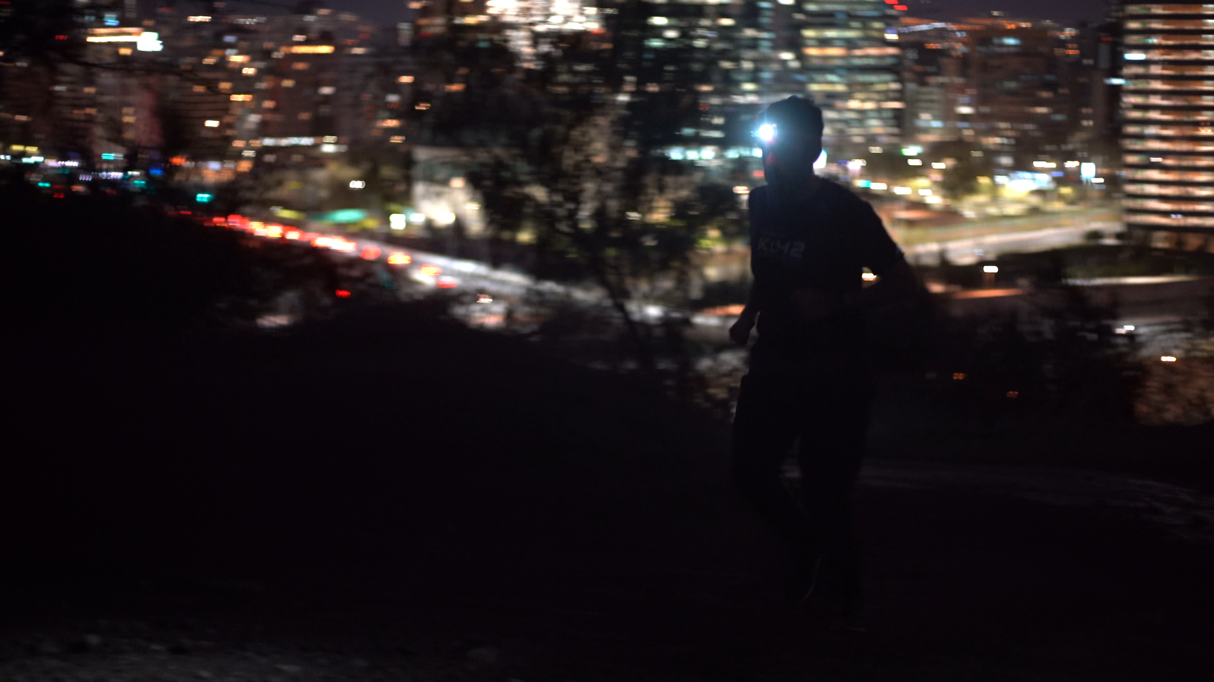 A person running outdoors at night in an urban area with blurred city lights in the background.
