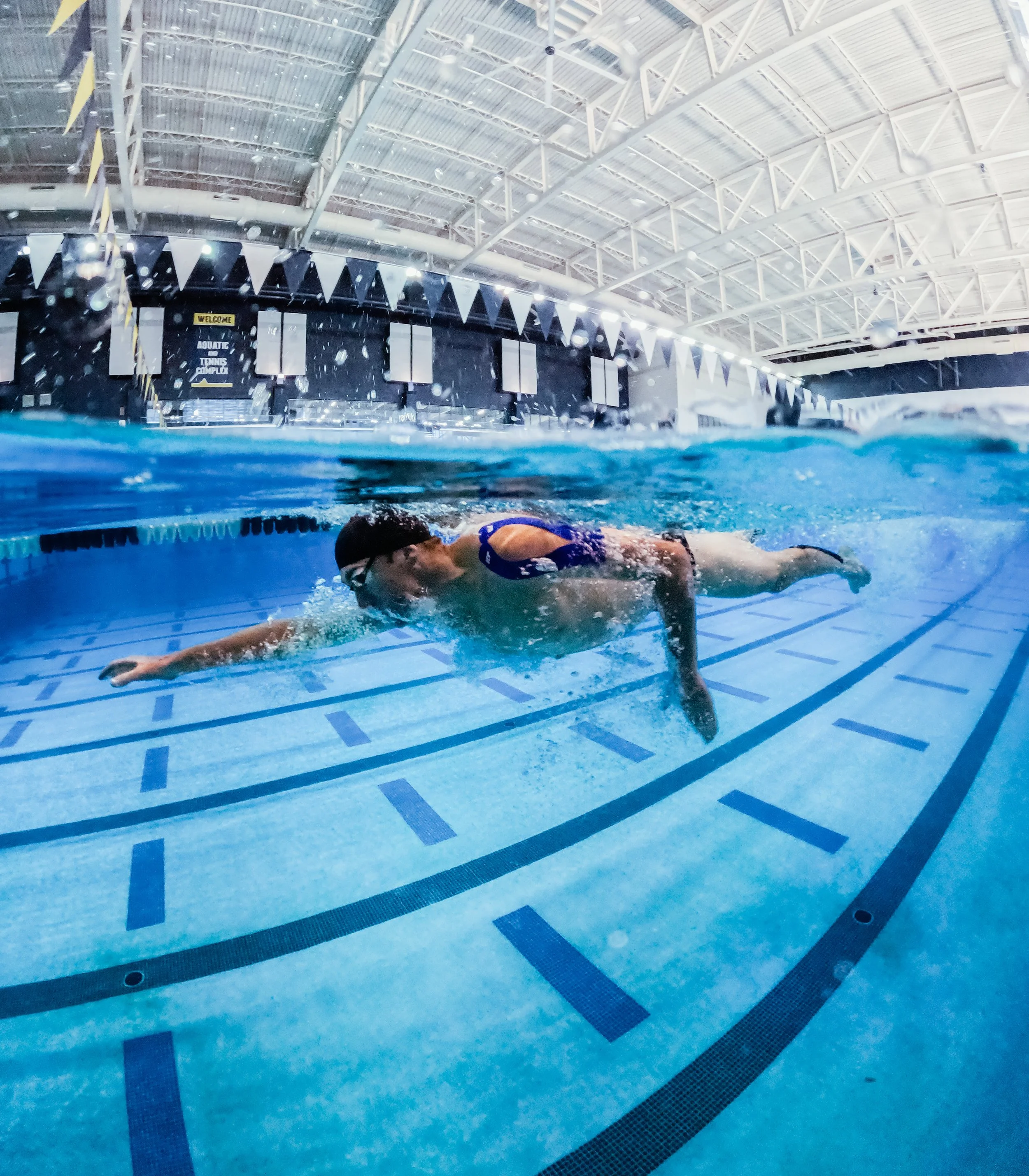Swimmer in a blue swimsuit swimming underwater in an indoor swimming pool.