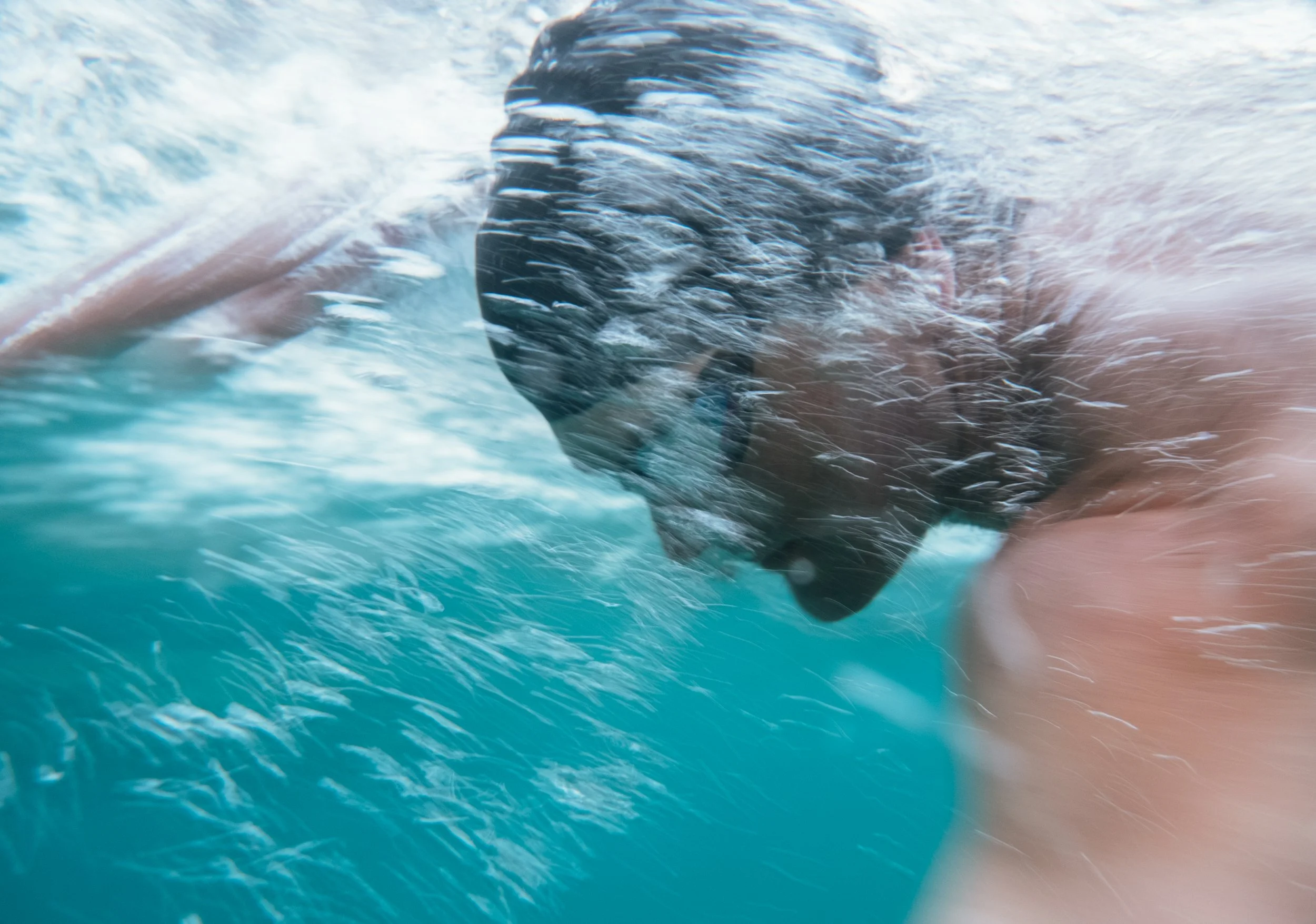 A person underwater with their head tilted downward and surrounded by bubbles, indicating they are swimming or diving.