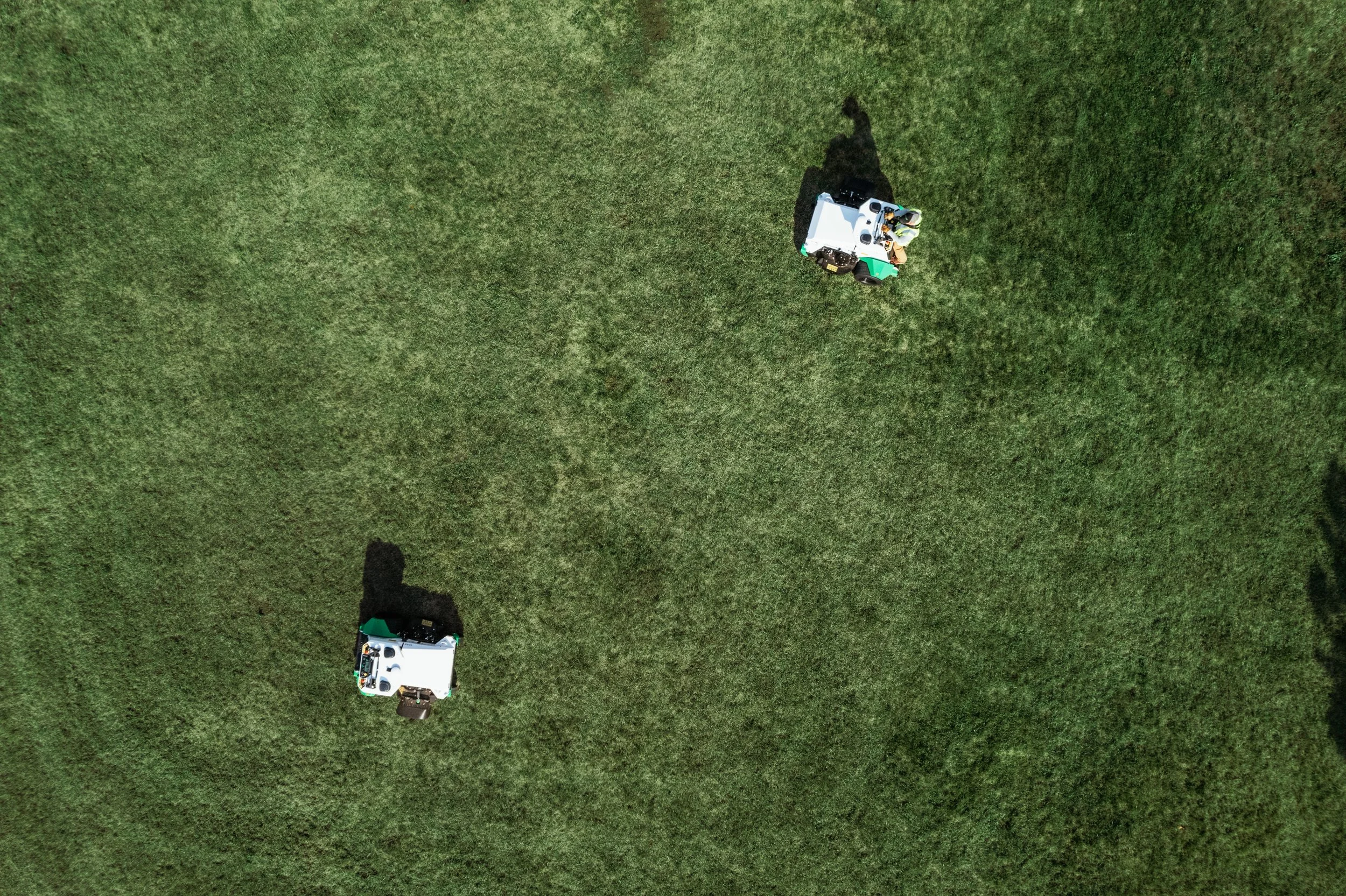Two tractors working on a green field, viewed from above during daytime.